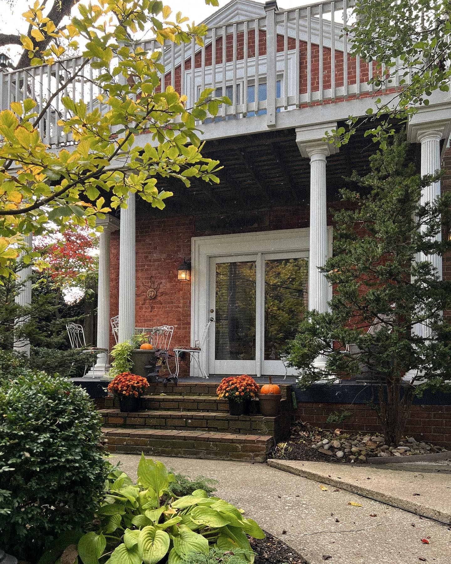 Brick house with white columns, balcony, and front door. Autumn foliage and pumpkins decorate the entrance.