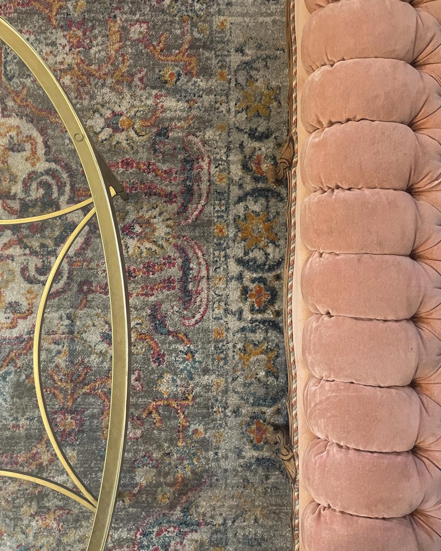 Gray patterned rug next to a pink, button-tufted upholstery. A gold-toned curved metal frame is partially visible.