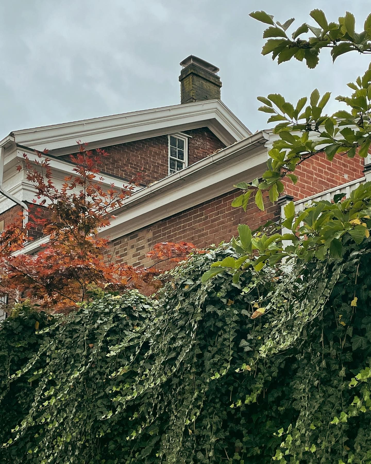 Brick building with white trim, green ivy, and red/orange foliage under a cloudy sky.