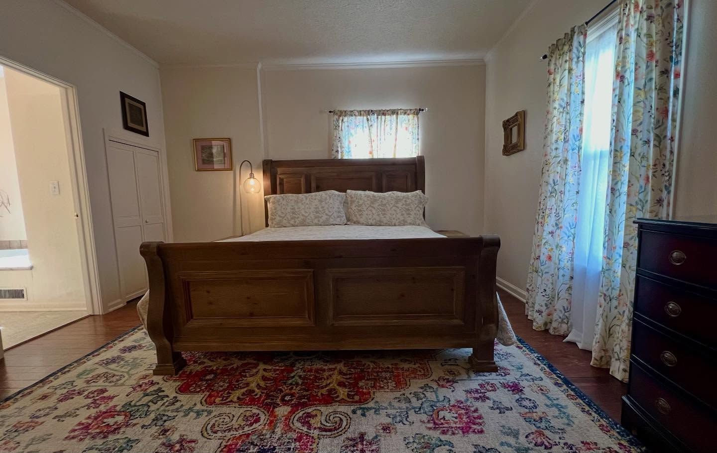Bedroom with wooden bed, floral rug, and curtains.