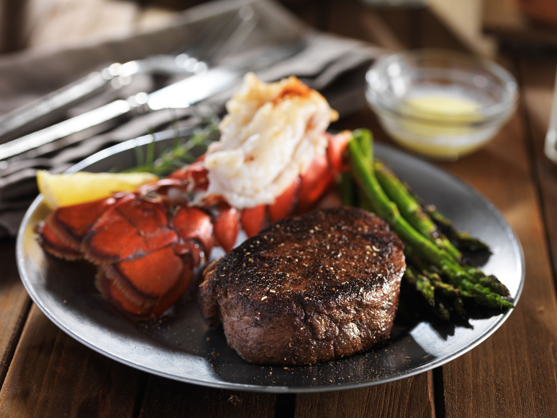 Surf and turf: Grilled steak and lobster tail with asparagus, lemon, and butter on a plate.