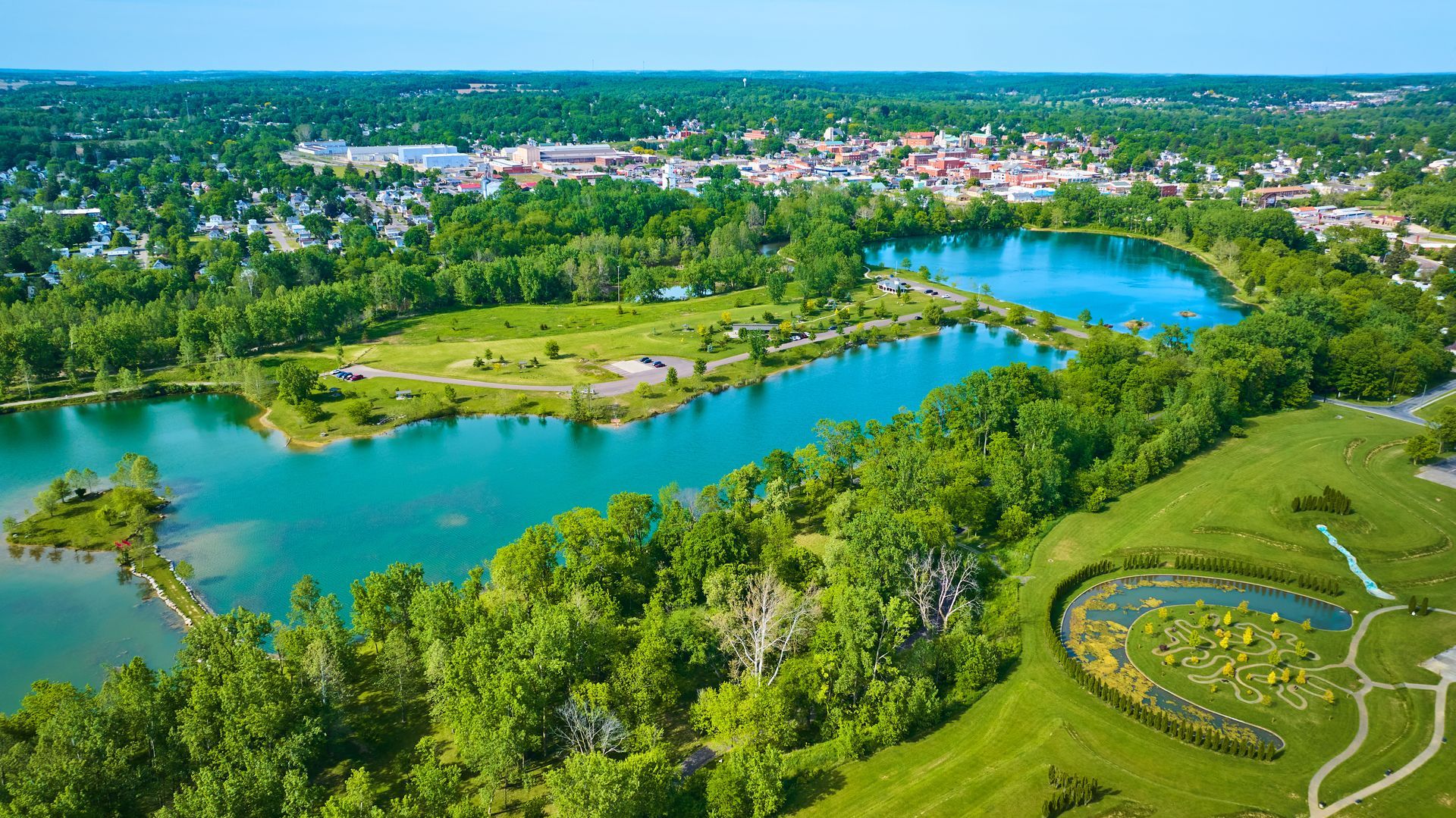 Aerial view of a bright blue lake surrounded by lush green trees and a town in the distance.