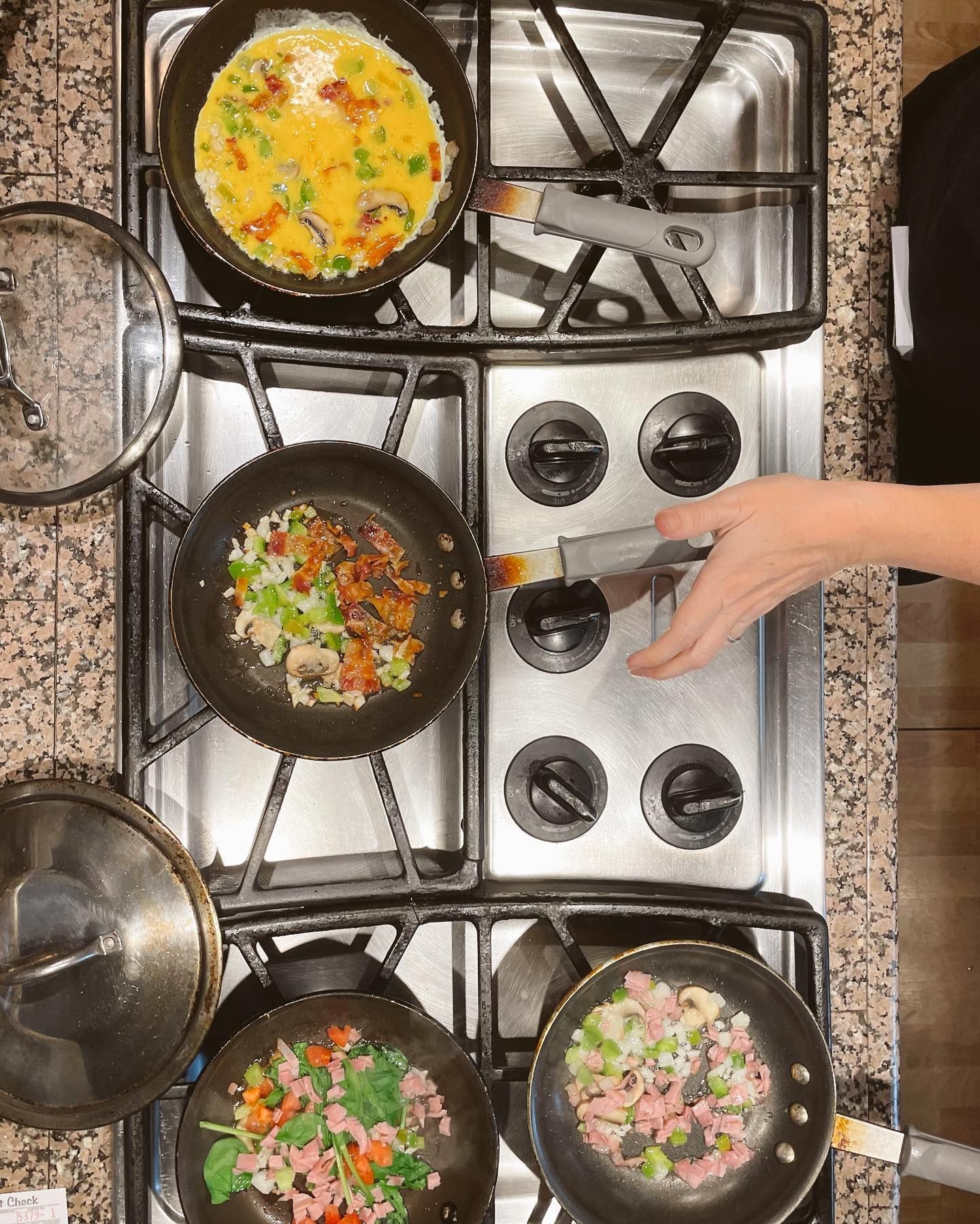 Overhead view of stovetop with four pans containing food; a hand adjusts a burner.