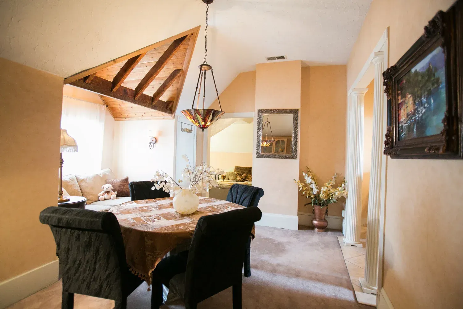 Dining room with table and chairs under a wood-beamed ceiling; archway leads to living area.