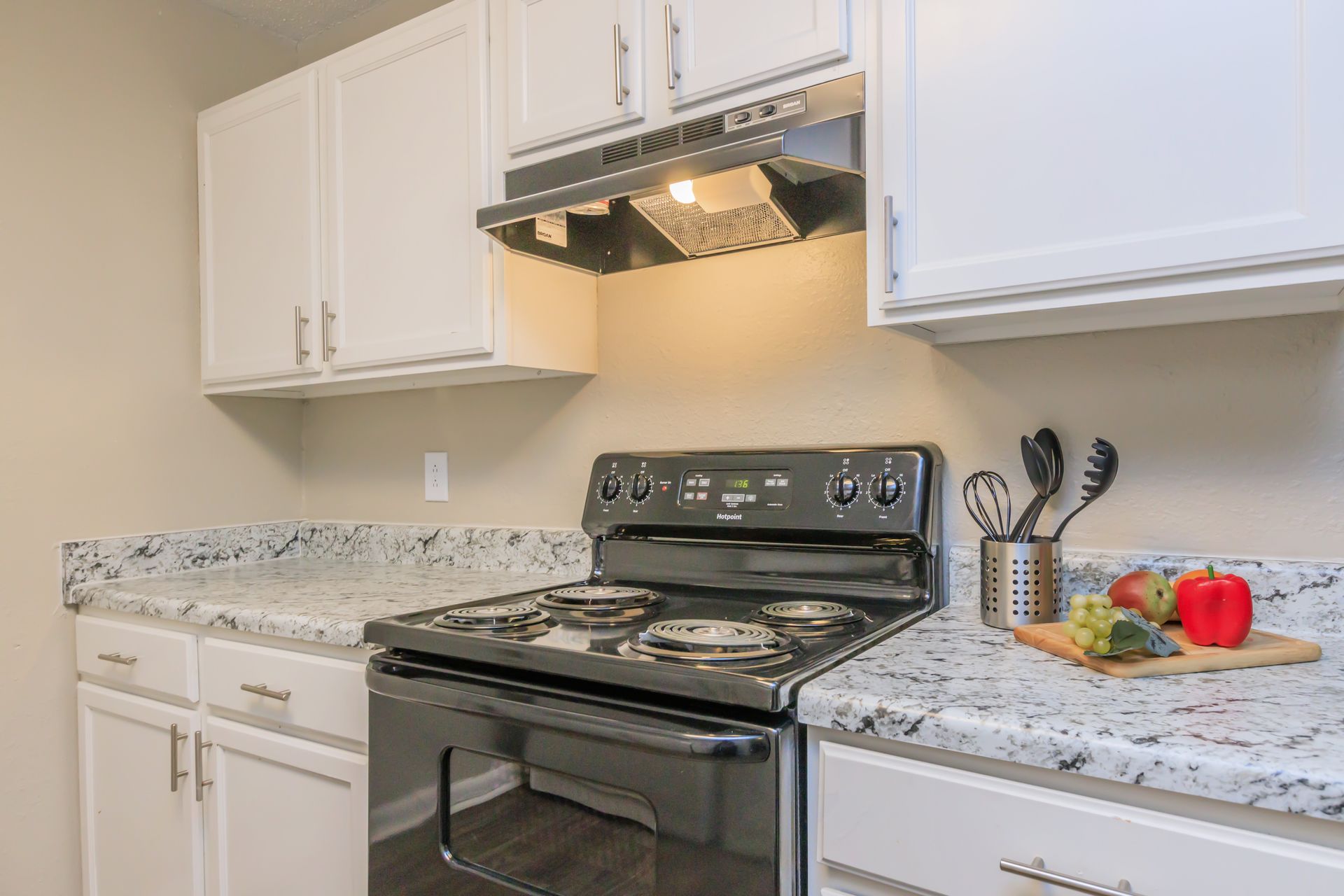 A kitchen with a stove , oven , microwave and white cabinets.