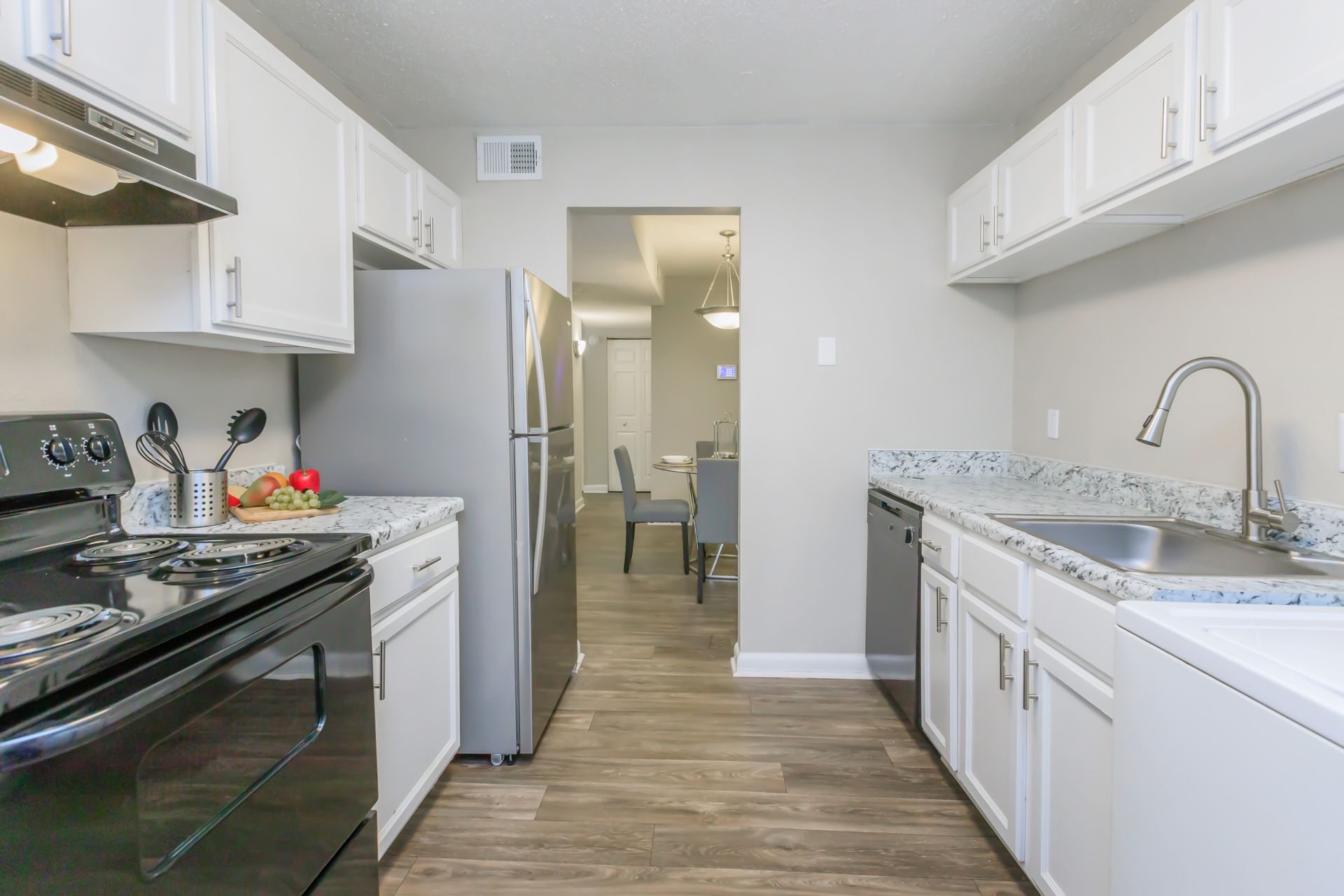A kitchen with white cabinets , stainless steel appliances , a refrigerator and a sink.
