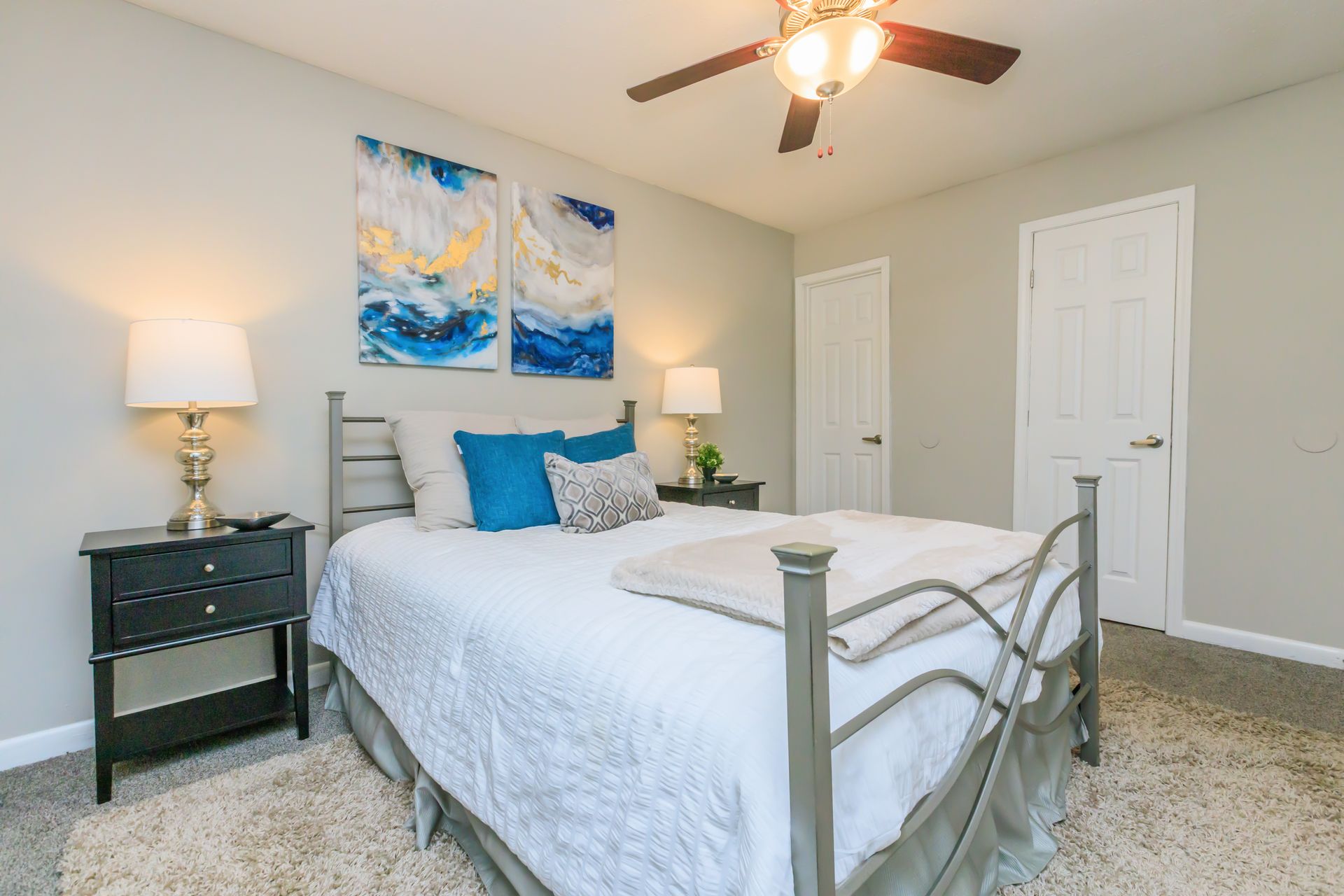 A bedroom with a bed , nightstand , lamps and a ceiling fan.