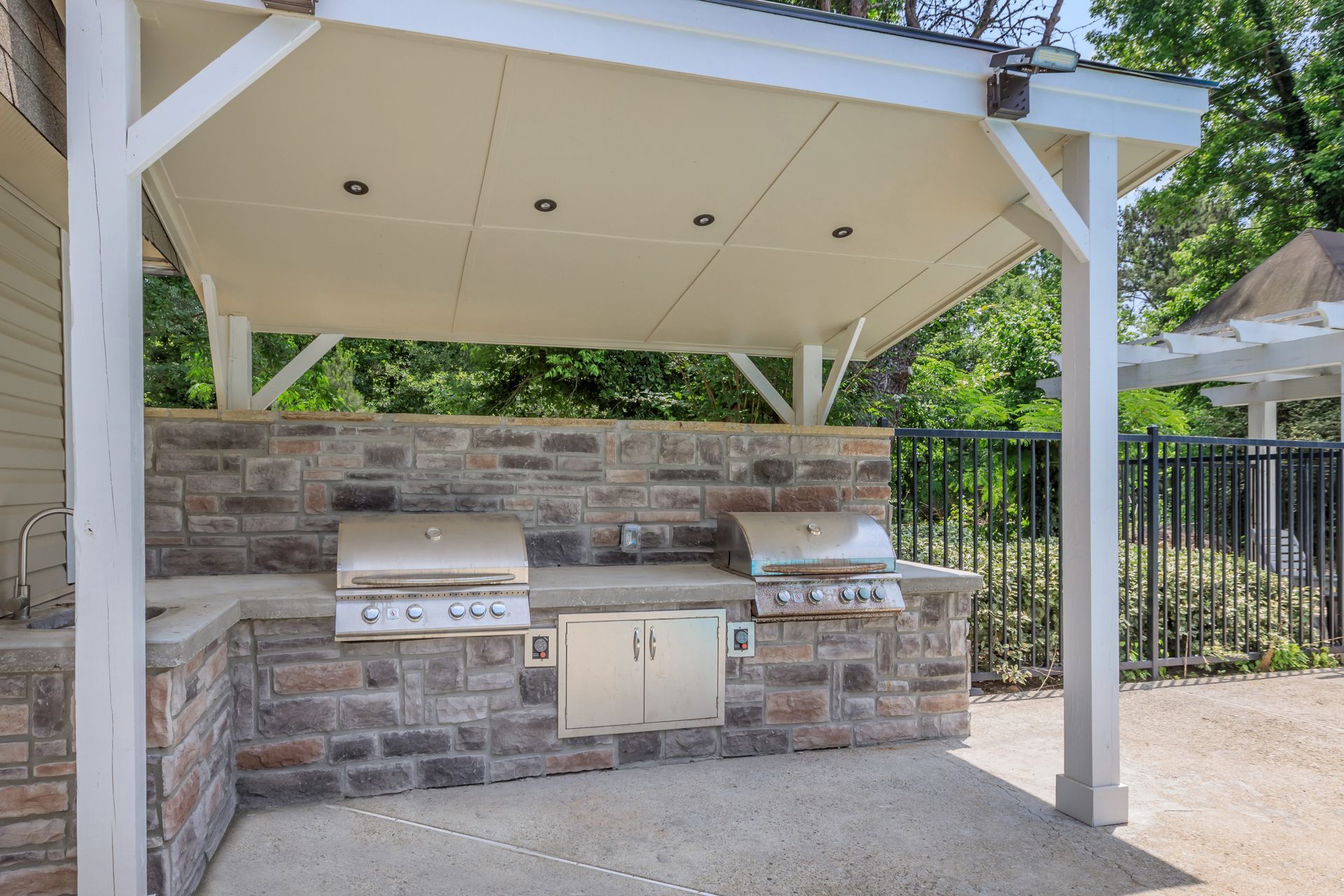 An outdoor kitchen with a grill under a pergola