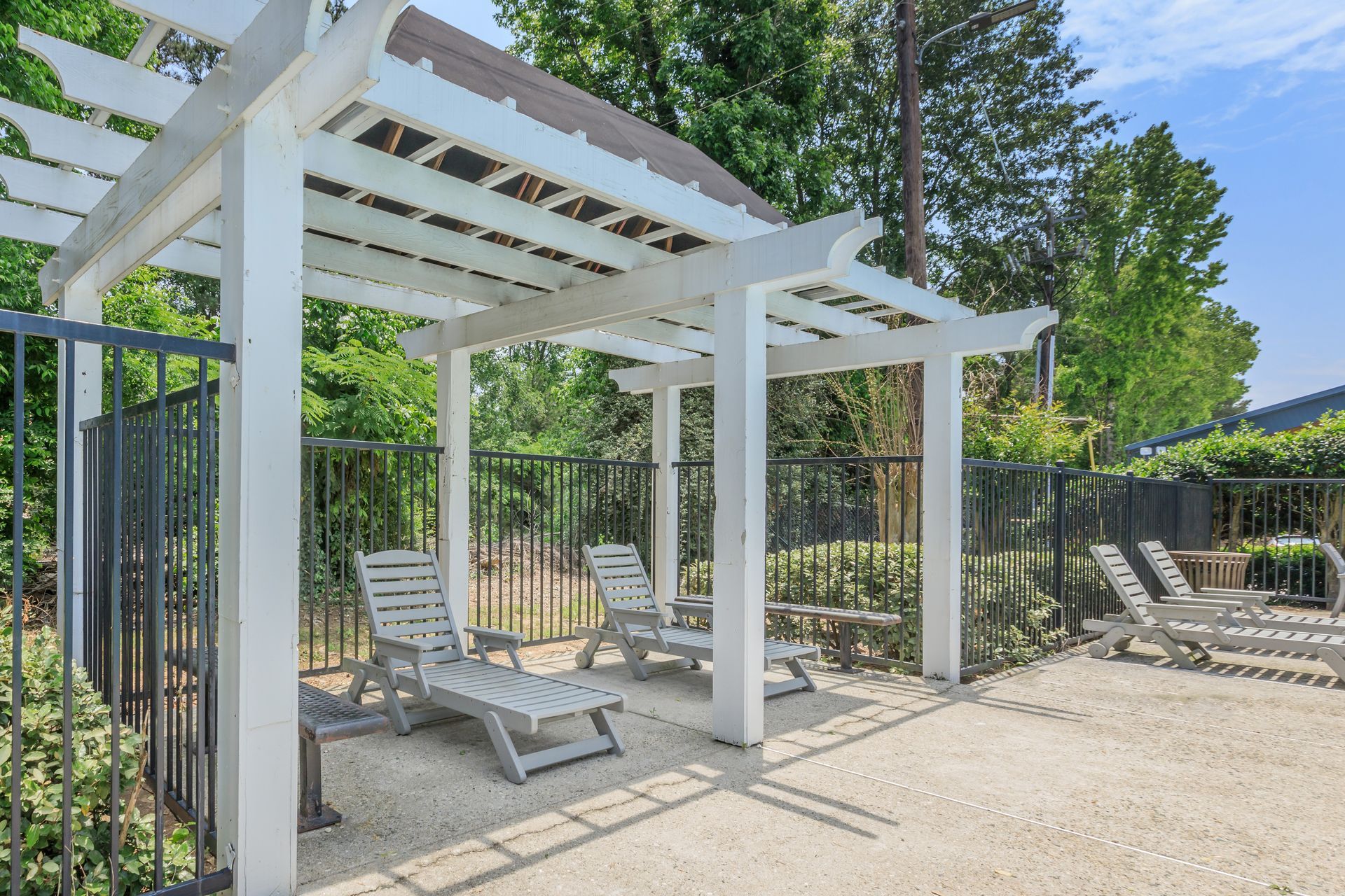 A white pergola with lawn chairs underneath it.
