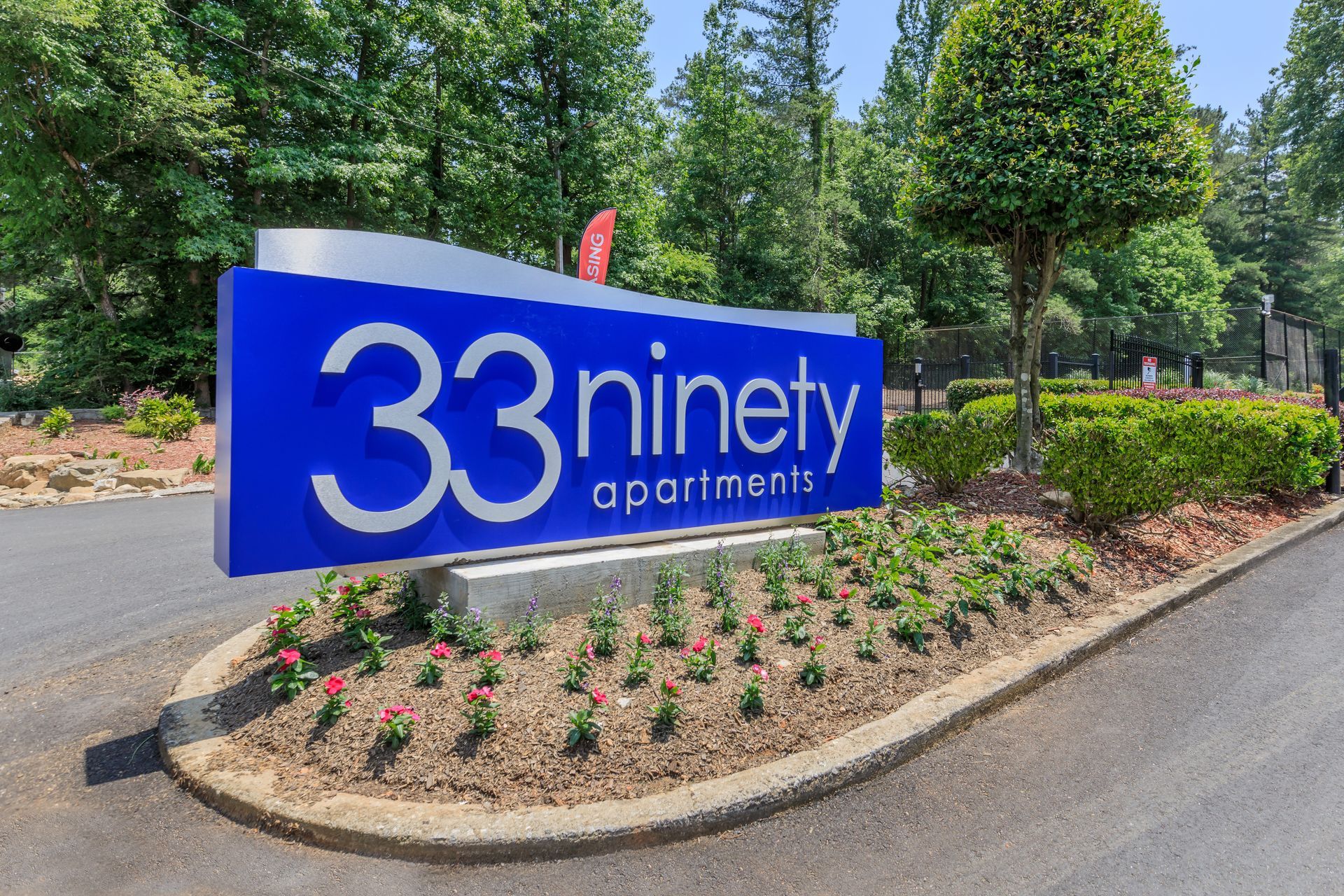 A blue sign for 33 ninety apartments is surrounded by flowers and trees.