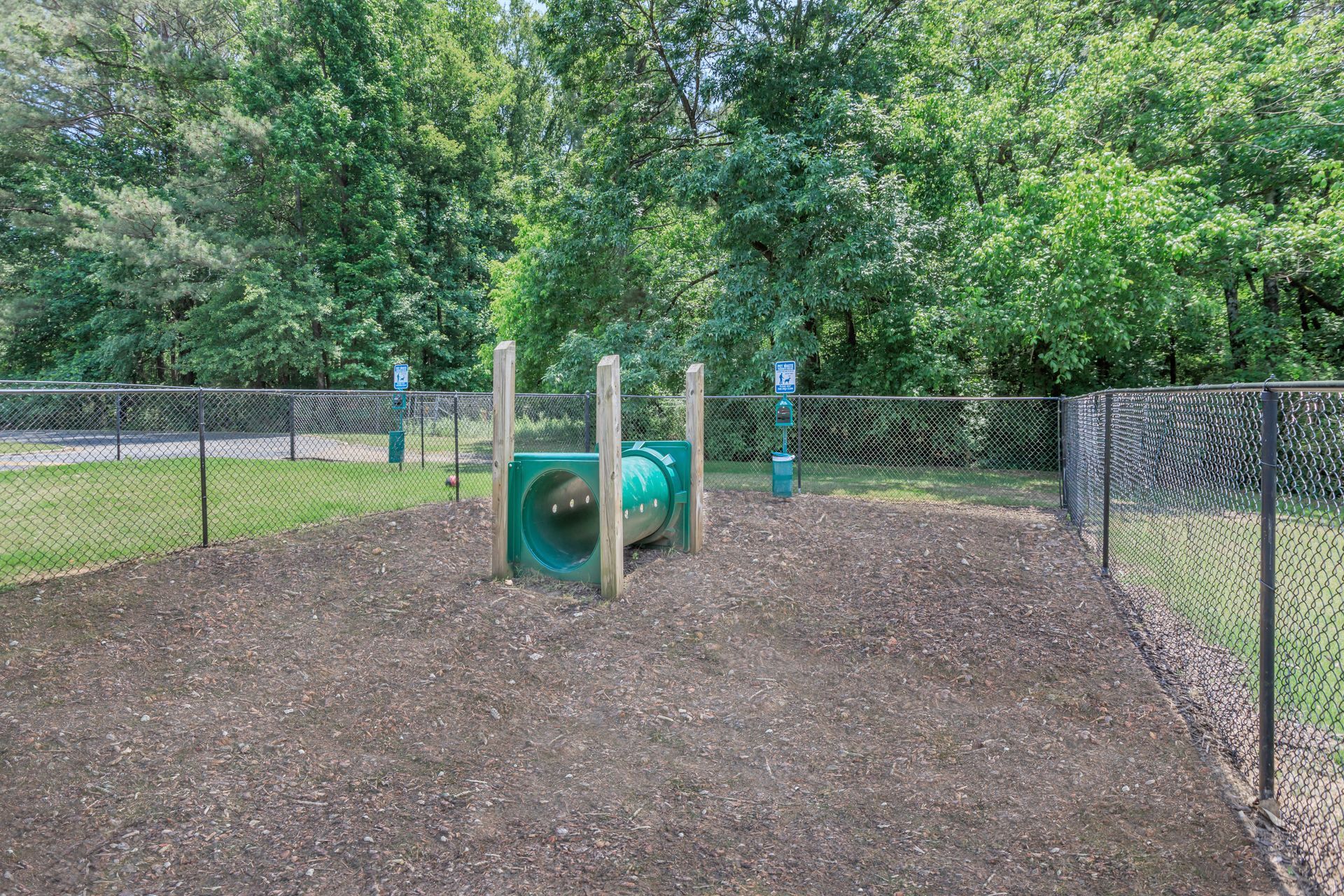 A dog park with a green tunnel and a chain link fence.