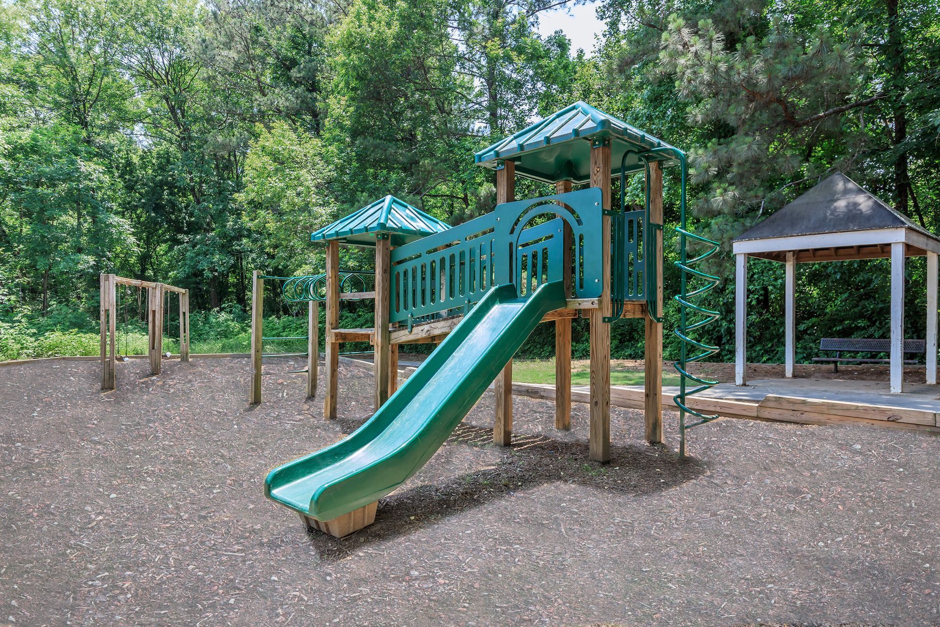 A green slide is in the middle of a playground in a park.