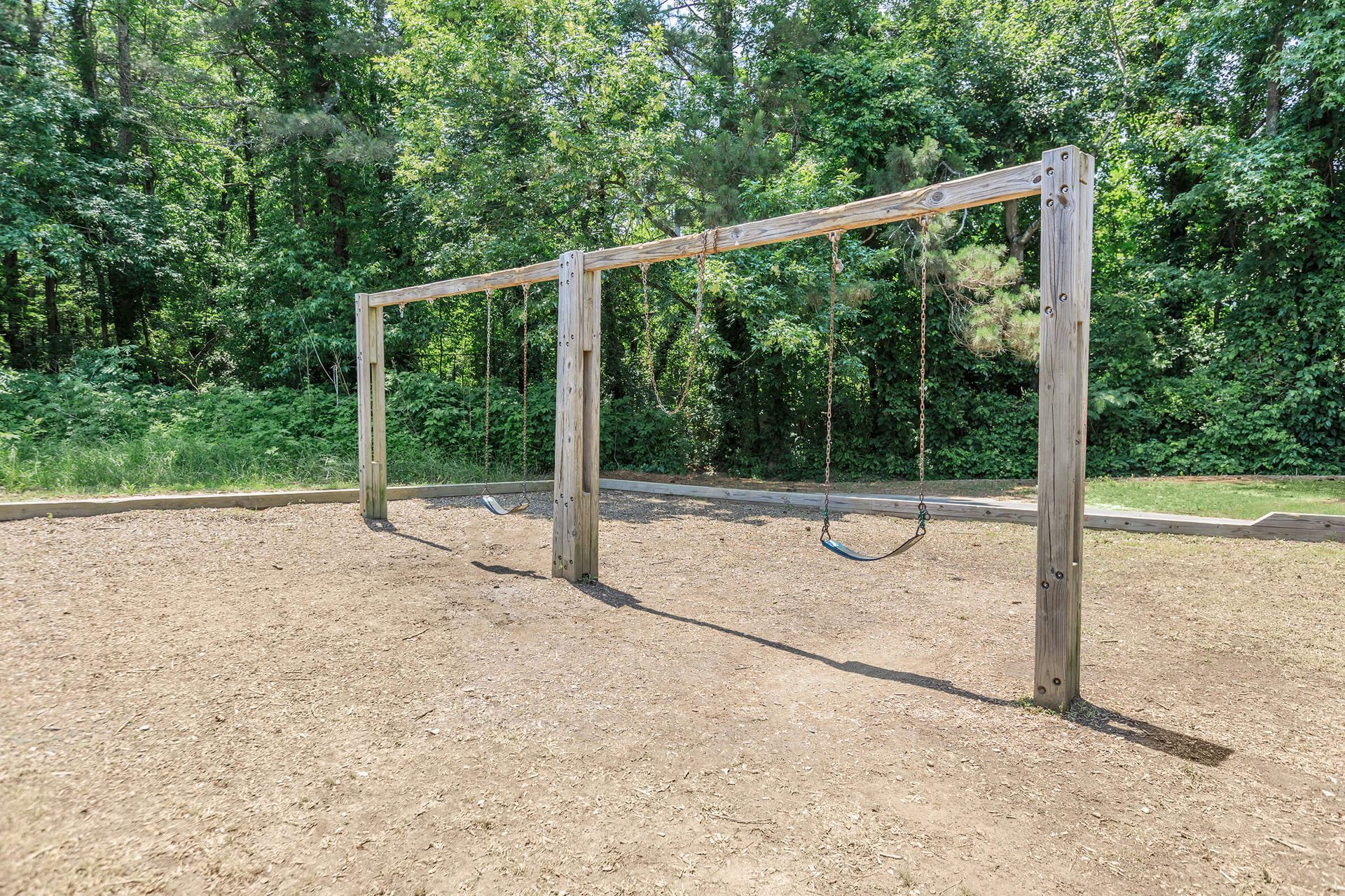 A wooden swing set in a playground with trees in the background.