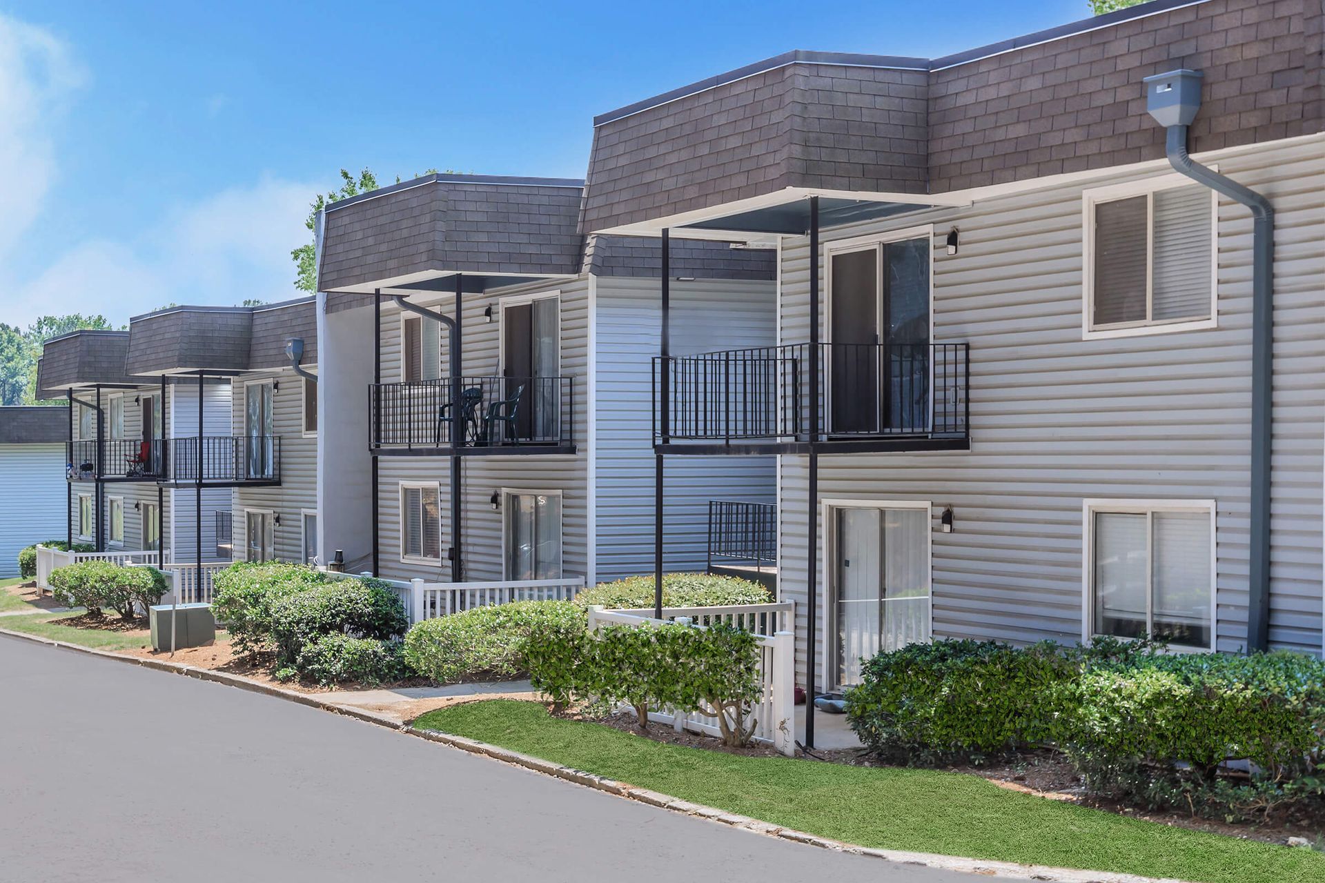 A row of apartment buildings with balconies and shrubs in front of them.