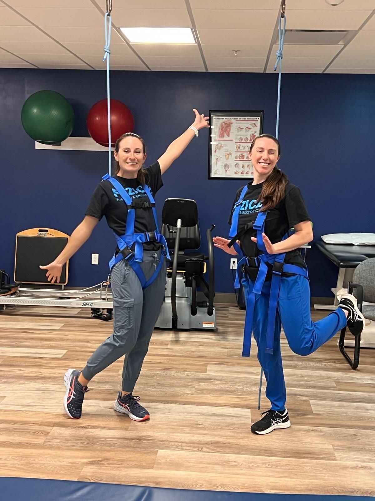 Two women wearing blue harnesses are standing next to each other in a gym.