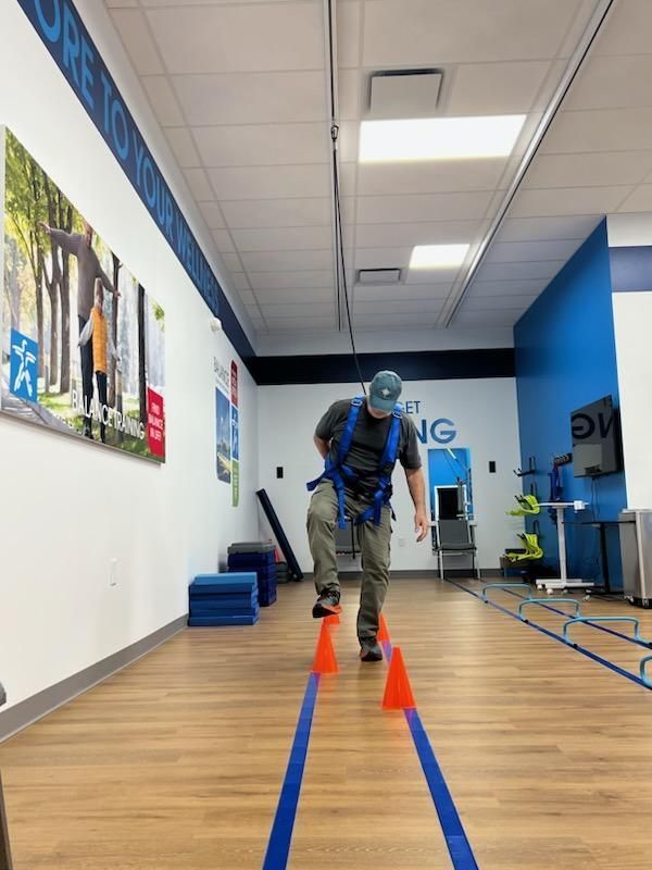 A man wearing a safety harness is walking between two cones in a gym