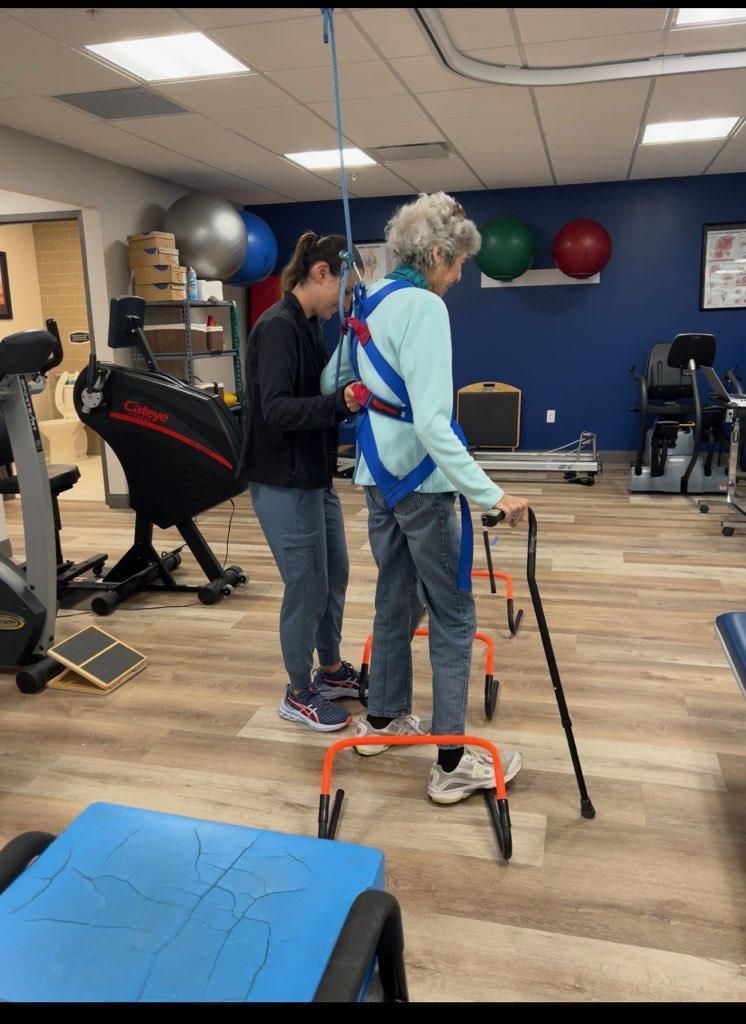 A woman is helping another woman with a walker in a gym