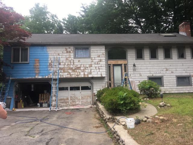 A house is being painted blue with a ladder in front of it.