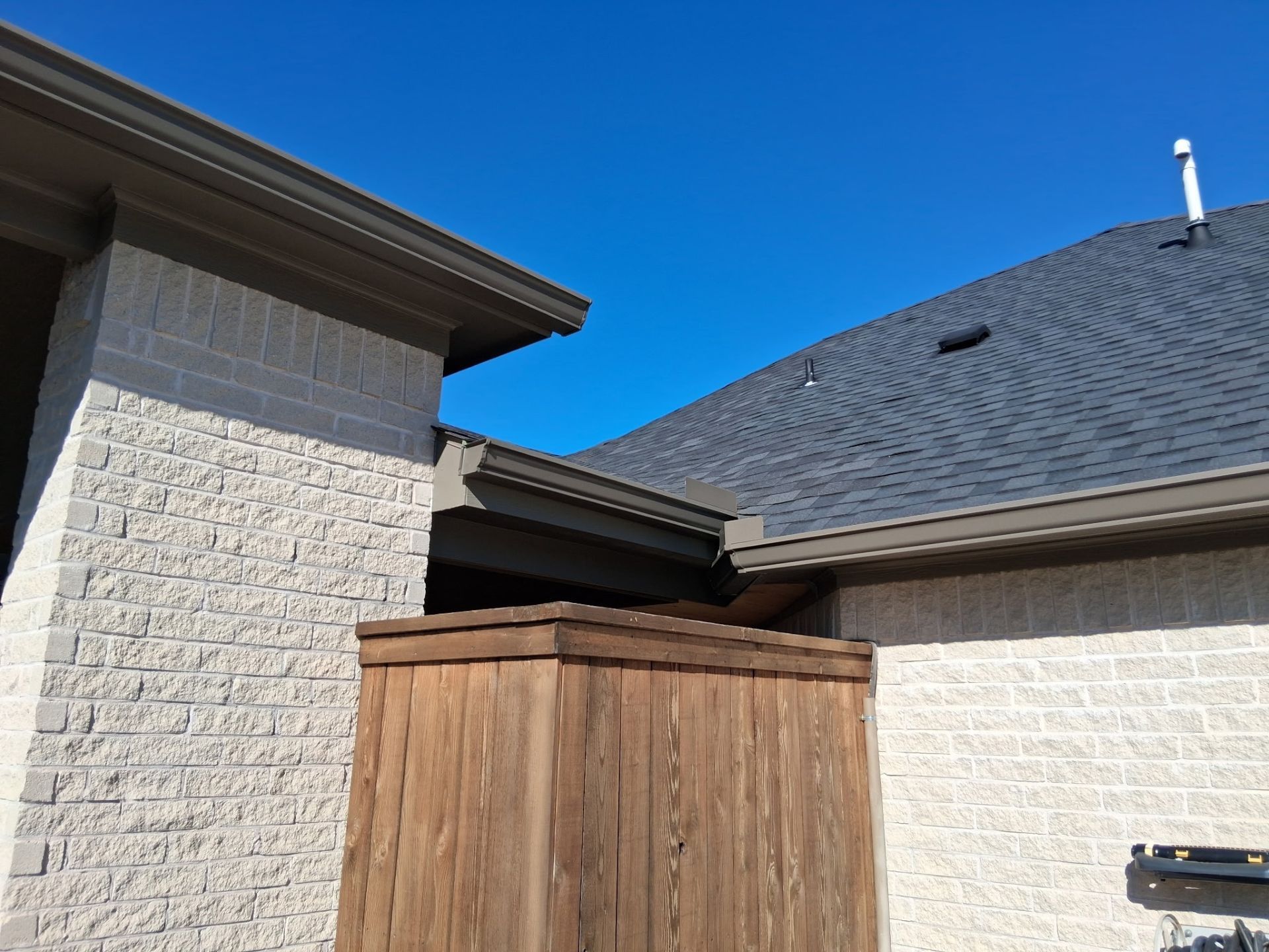 Exterior view of buildings with gray roof, brick walls, and wooden fence against a blue sky.
