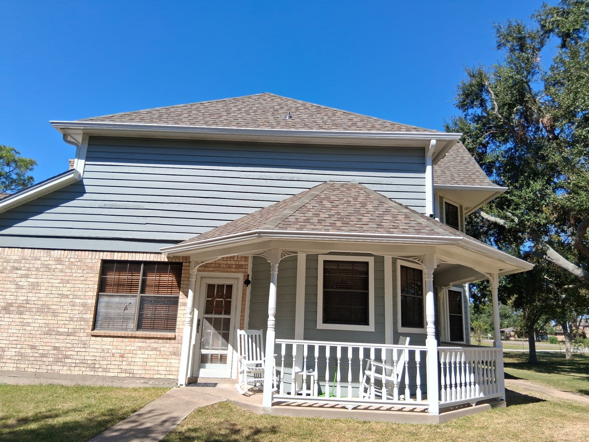 Two-story house with blue siding, brick, and a porch. Bright sunny day.