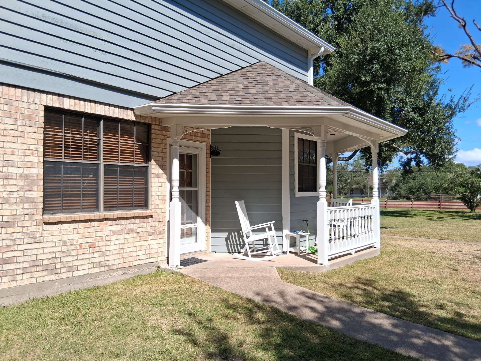 Porch with rocking chair and railing on a two-story house with brick and blue siding, sunny day.