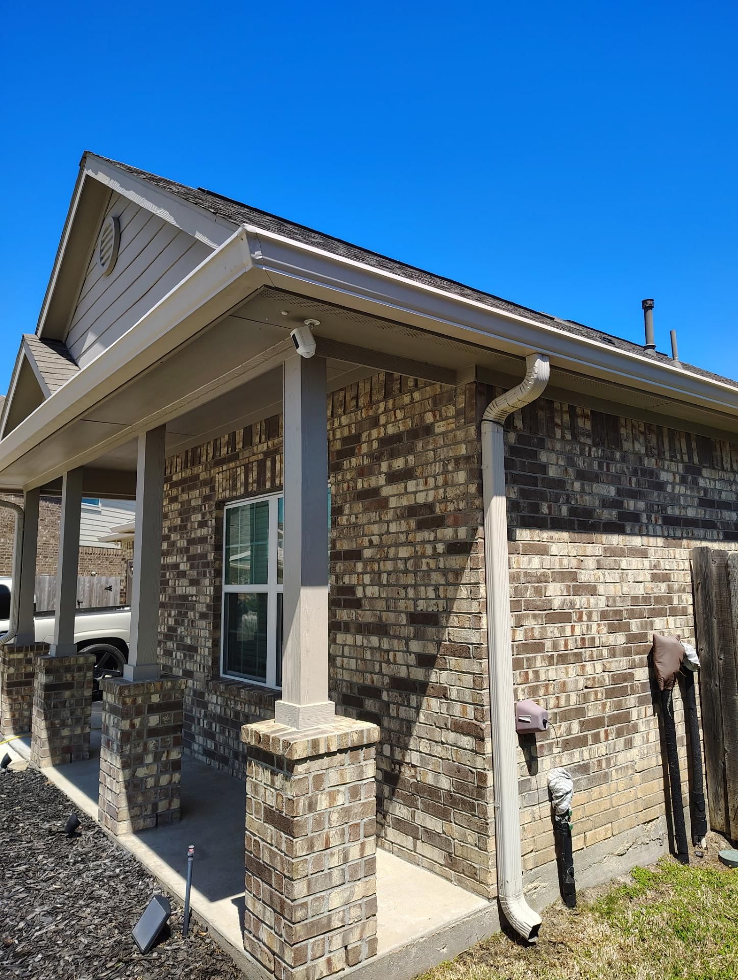 Brick house exterior with porch, tan trim, and a clear blue sky.