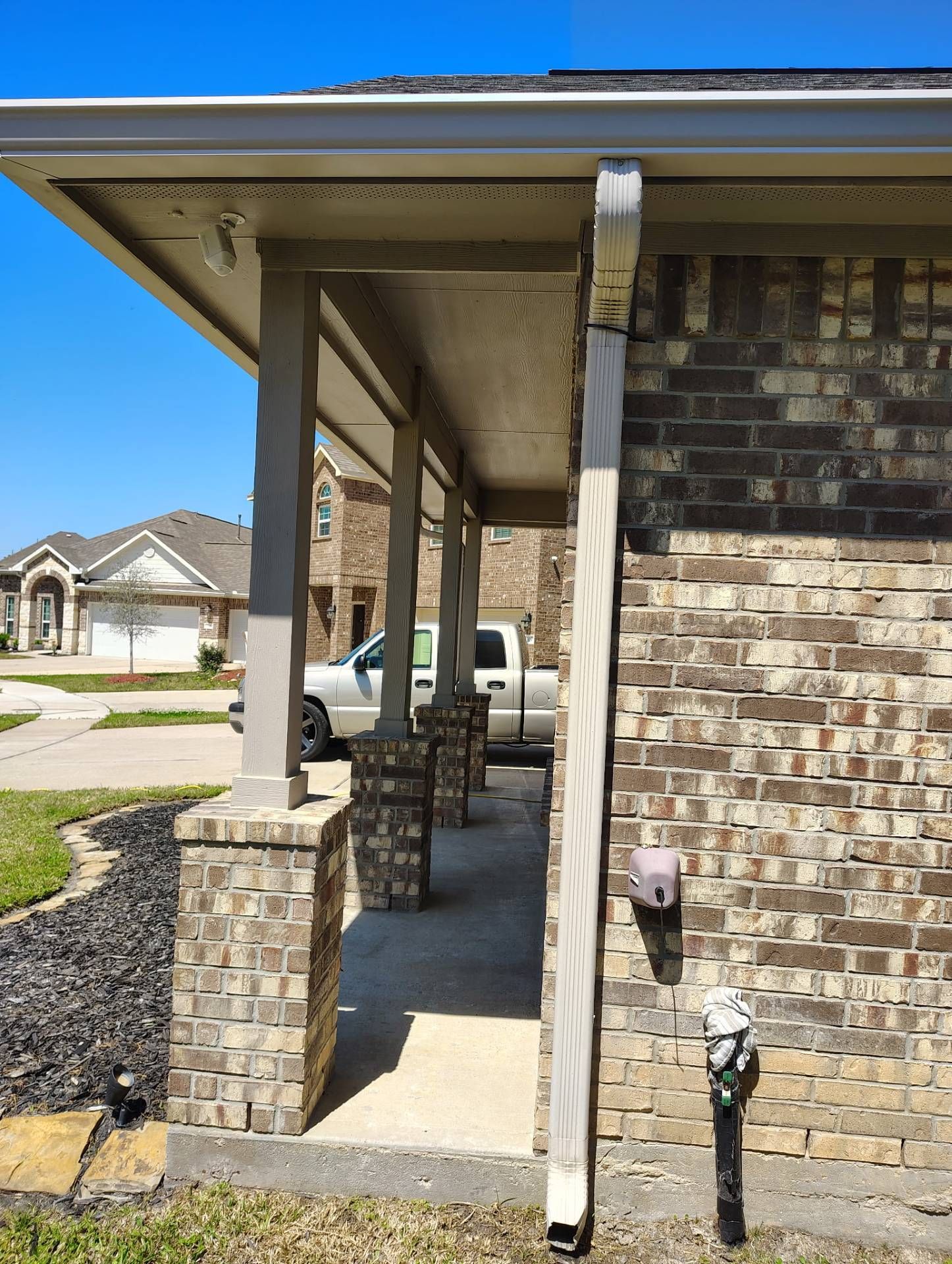 Covered brick porch with gray columns, gutter, and a house in the background on a sunny day.