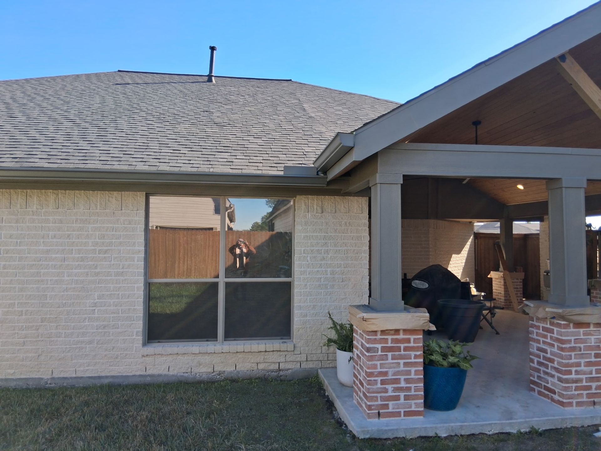 Exterior view of a brick house with a covered patio. A window reflects a fence.
