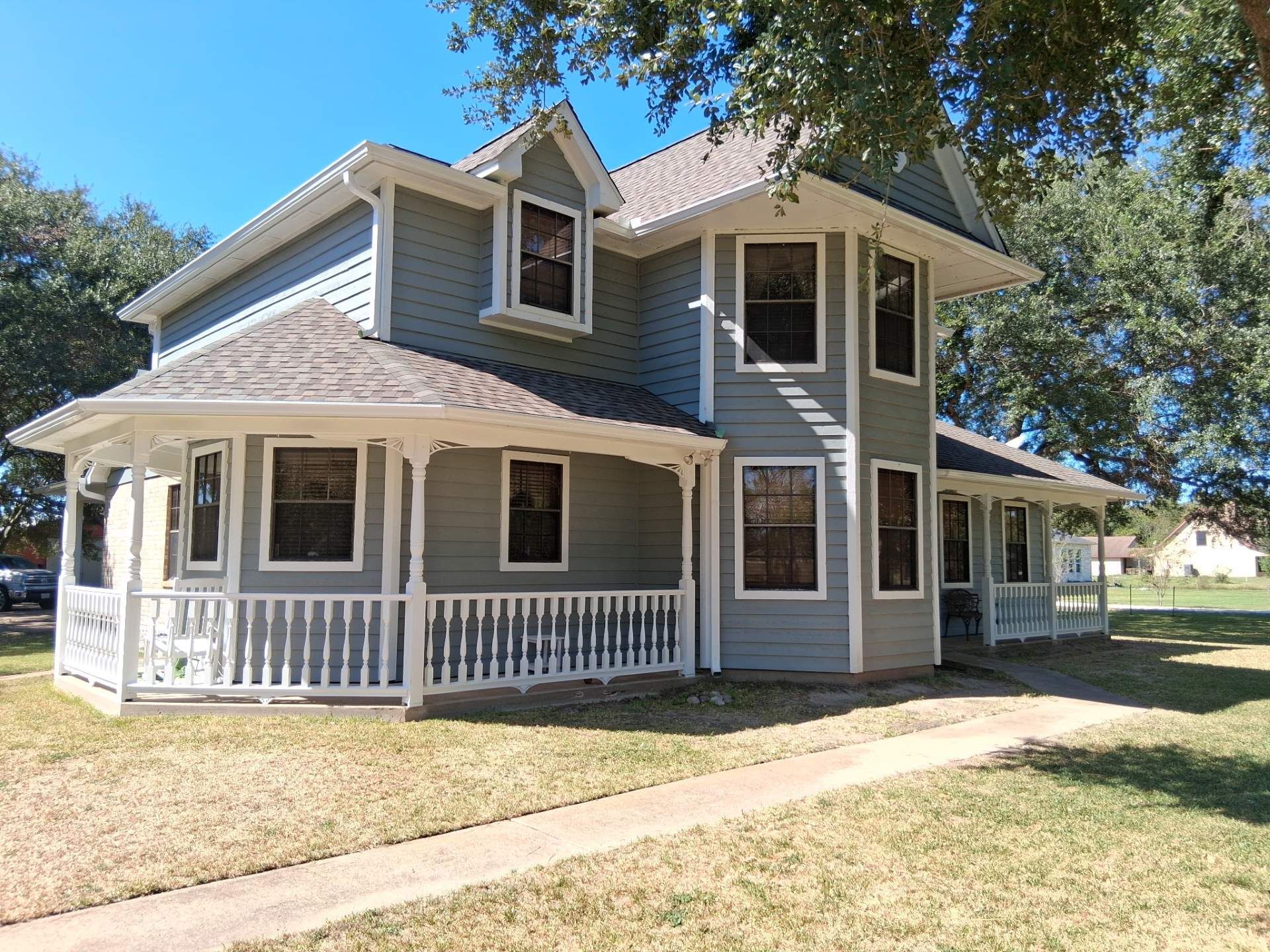 Two-story gray house with white trim, porch, and a dormer against a blue sky.