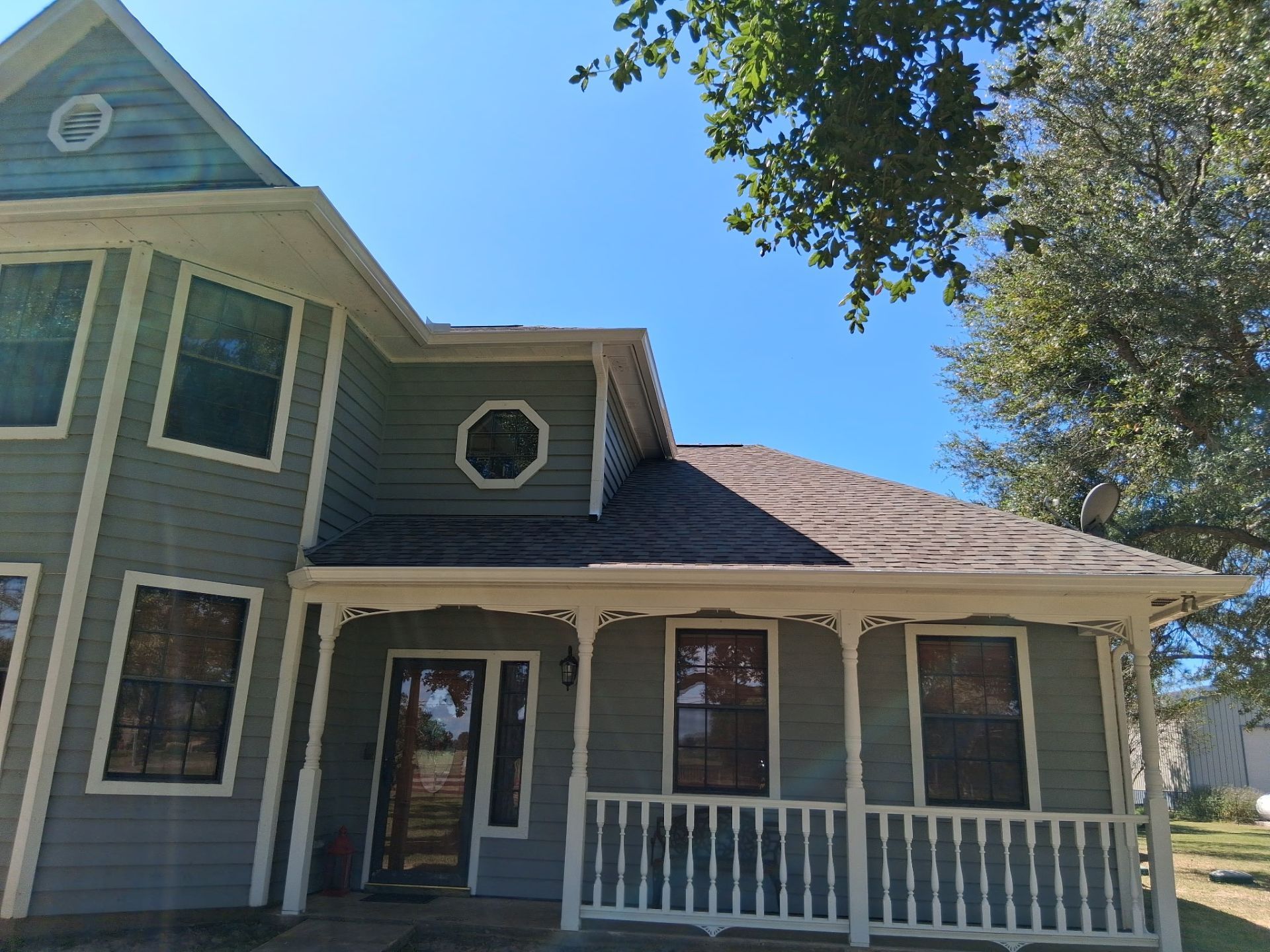 Two-story house with green siding, white trim, and porch. Clear blue sky and a tree are in the background.