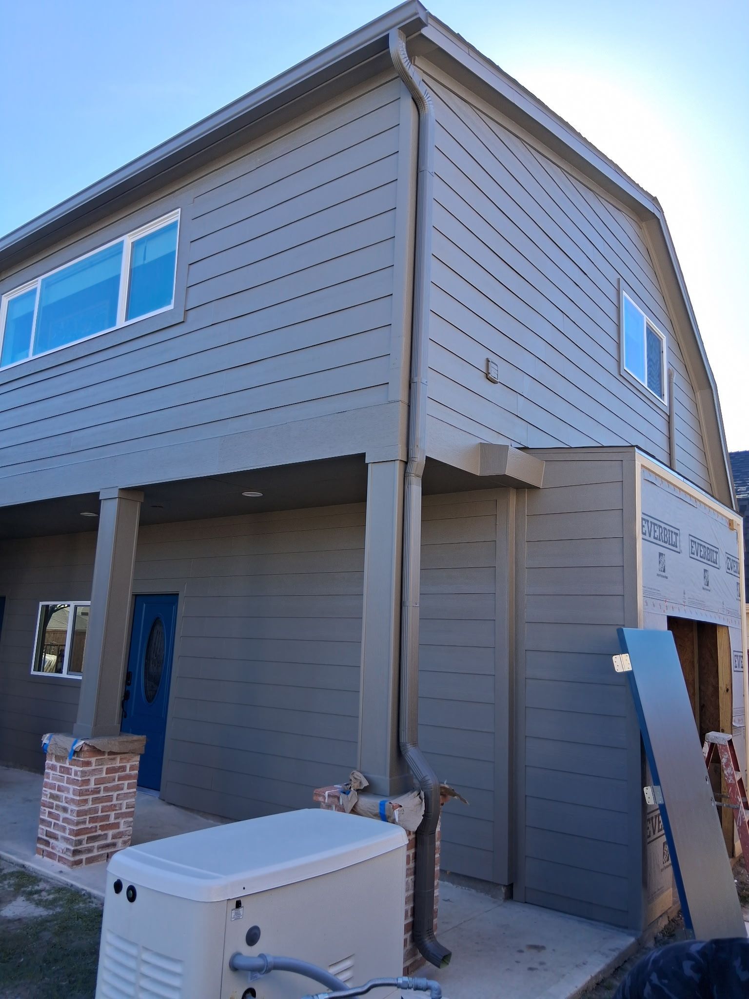Two-story building with gray siding, blue door, and tan trim. A generator sits in front.