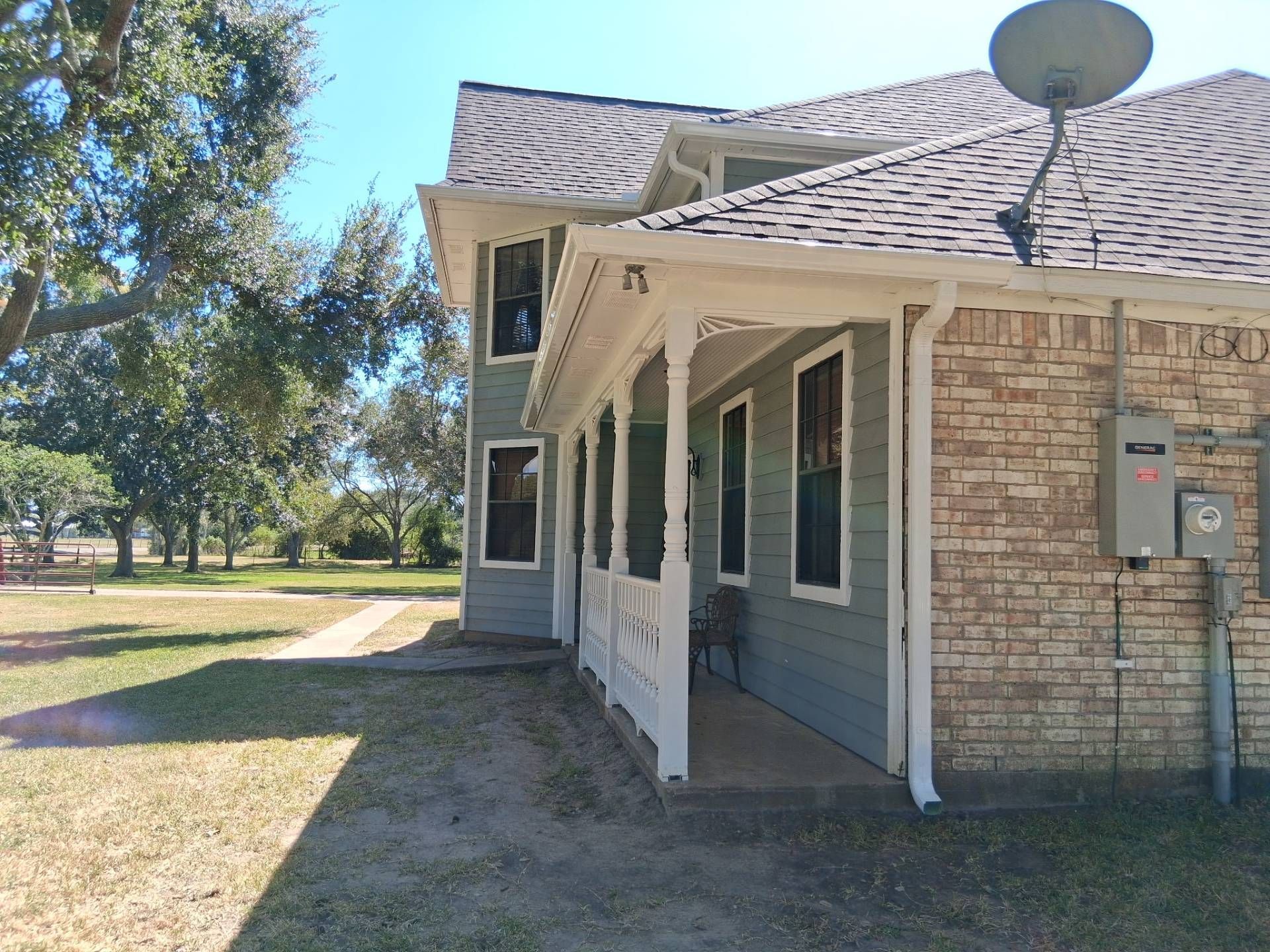 A two-story house with a porch. The house has light blue siding and a brick section. A satellite dish is attached.