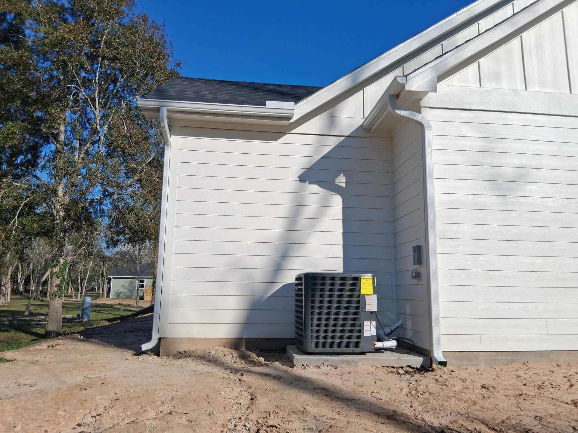 An air conditioning unit next to a white house with gutters on a sunny day.