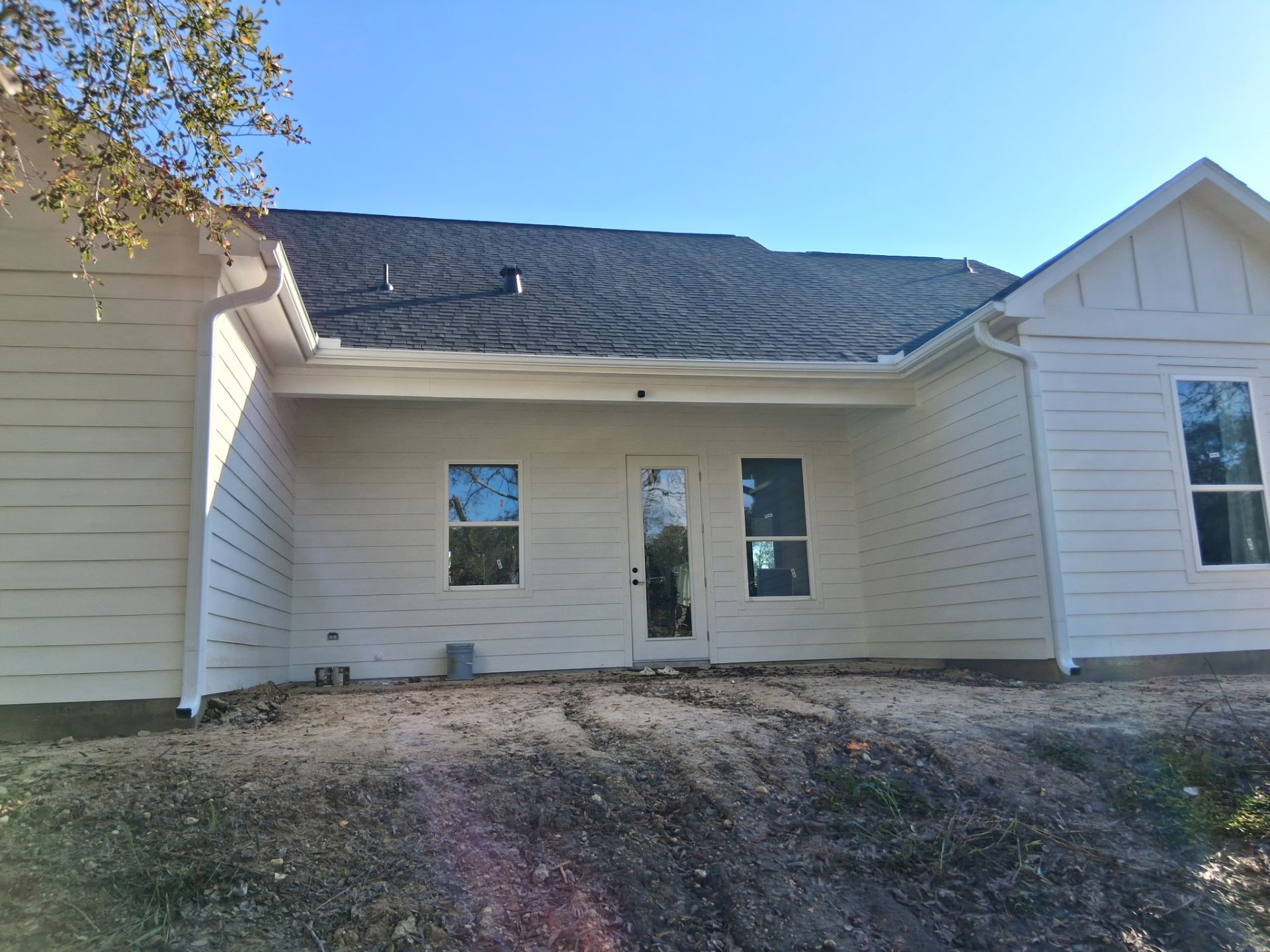 Exterior view of a house with white siding, windows, and a black roof on a sunny day.
