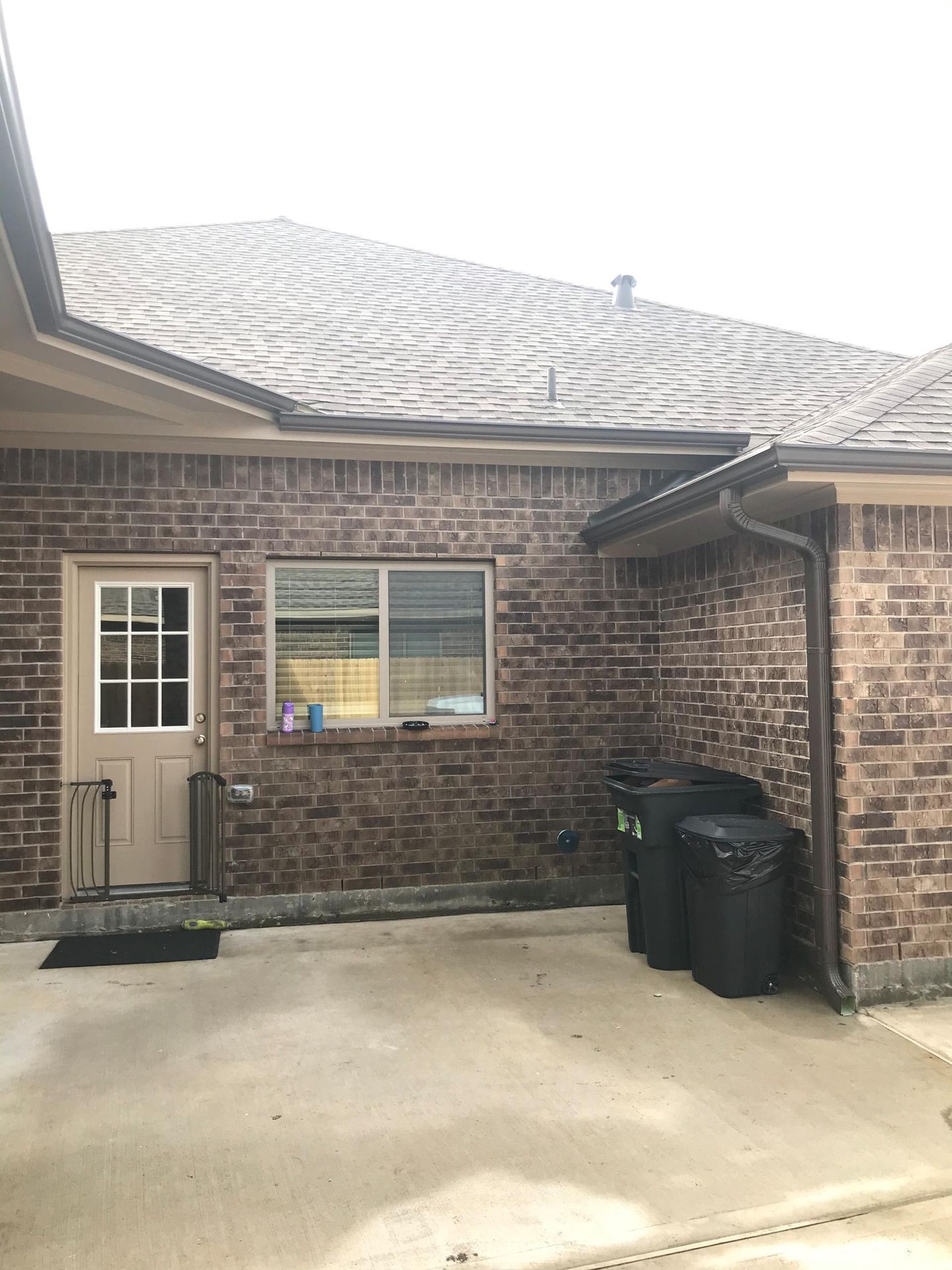 Brick building exterior with door, window, and trash cans on a concrete patio.