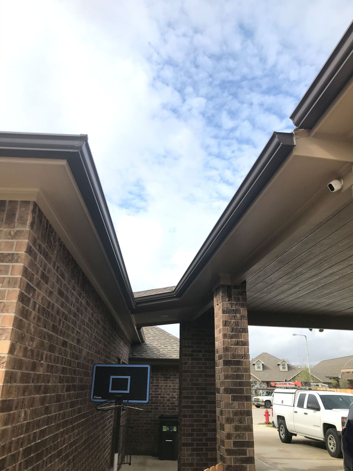 Brick buildings with brown gutters and cloudy sky. A basketball hoop stands in the front.