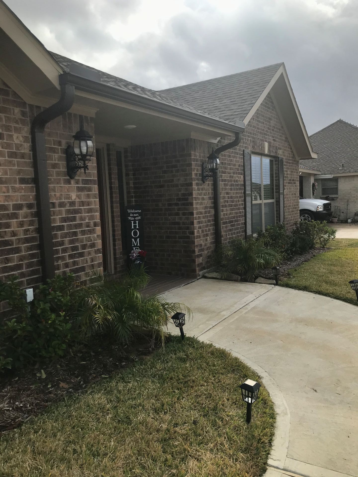 Brick home exterior with porch, lawn, and walkway. Brown roof, gutters, and trim.