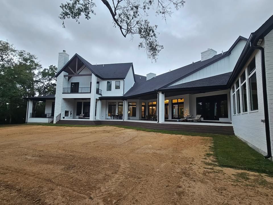 White house with black roof and trim on a cloudy day. Unfinished lawn in foreground.