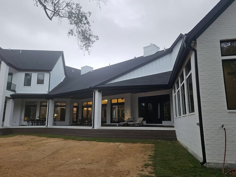 Exterior view of a white brick house with a dark roof and a covered patio, under a cloudy sky.