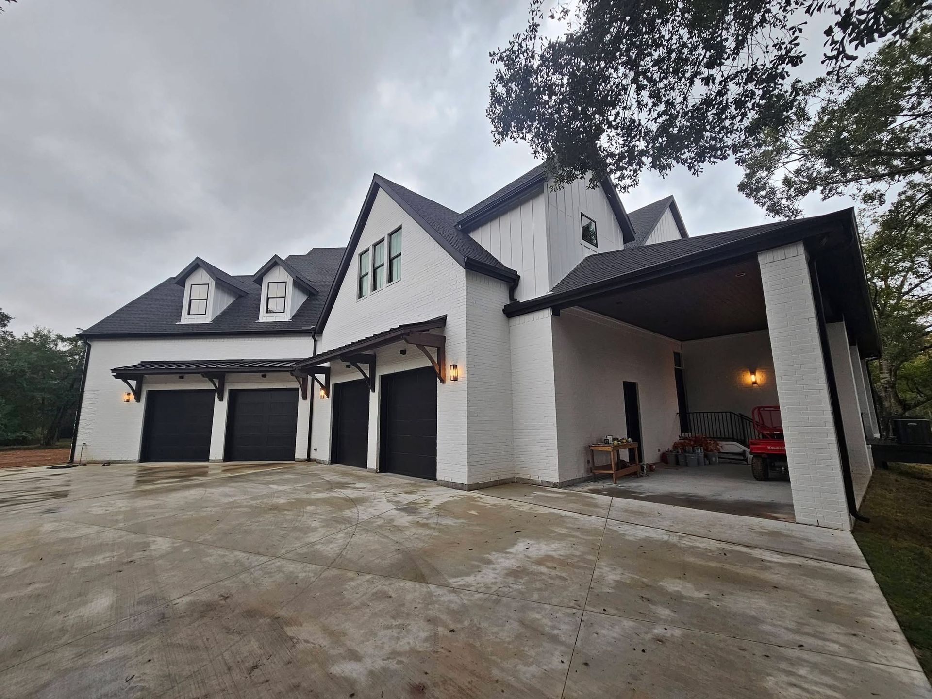 White house with black roof, garage doors, and accents. Driveway in front. Cloudy sky.