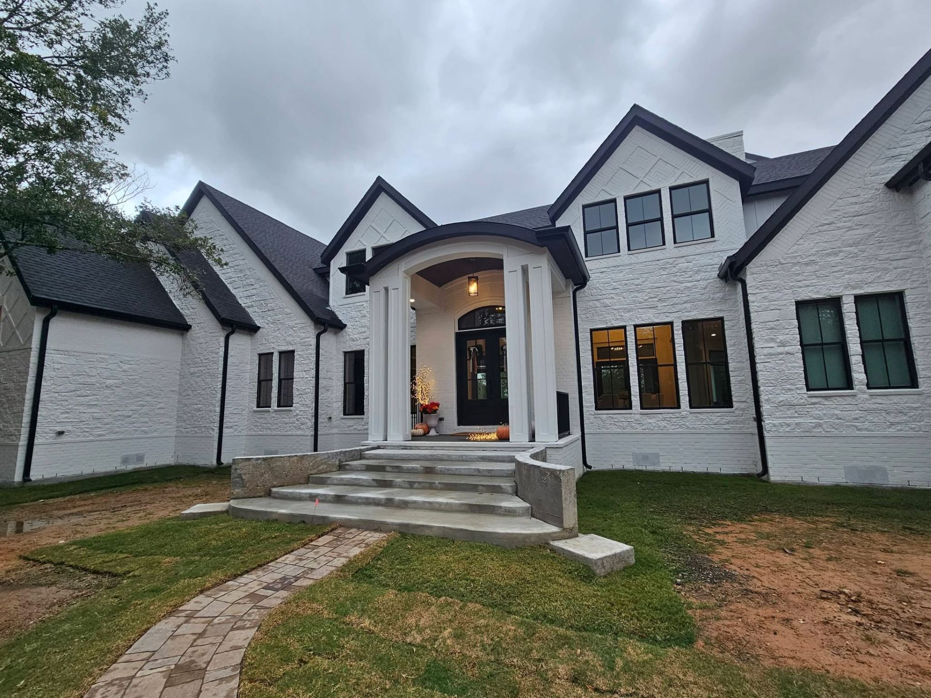 White brick house with black roof, windows, and front door, overcast day.