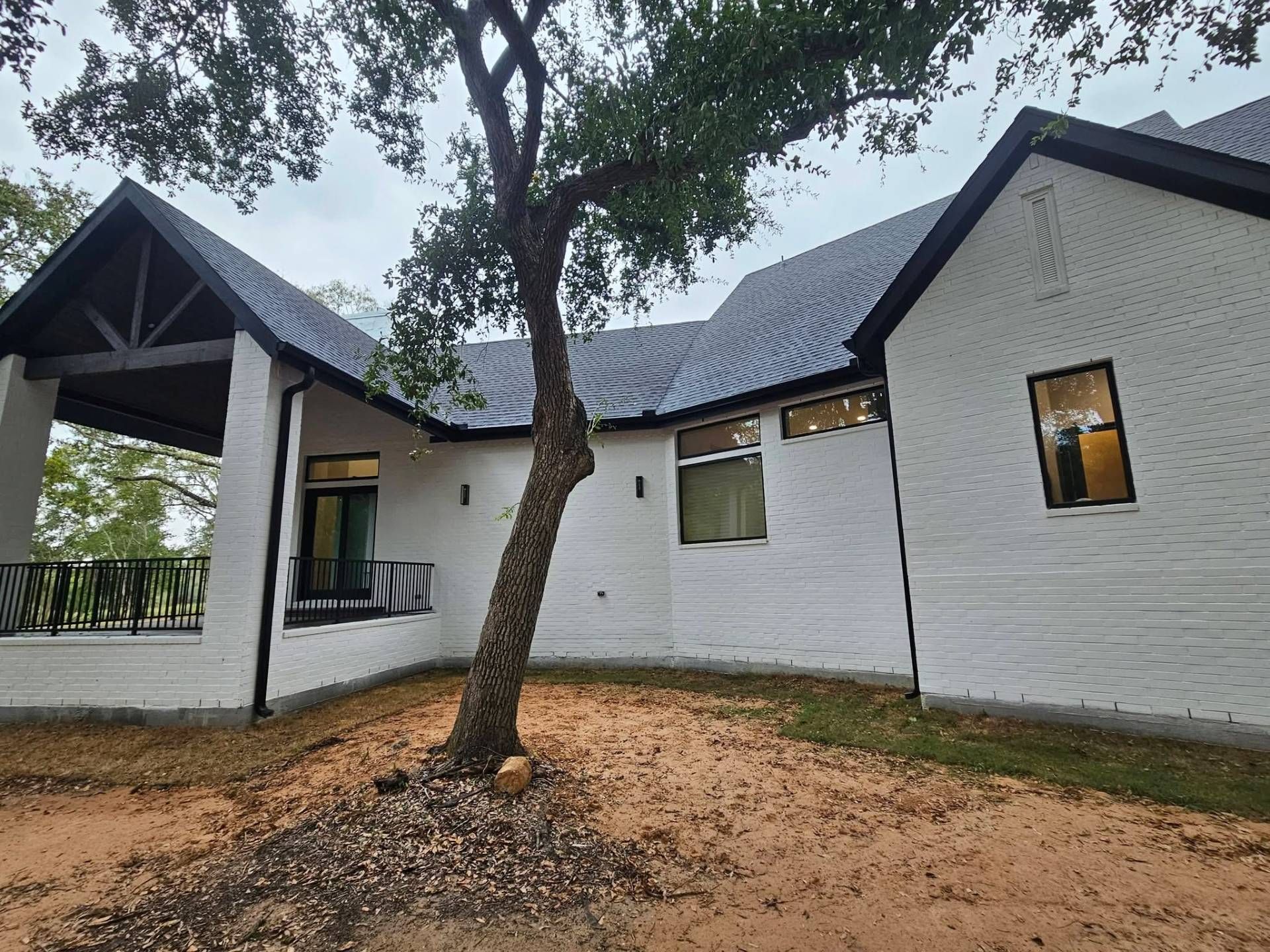 White brick house with black trim and a dark roof; tree in front.