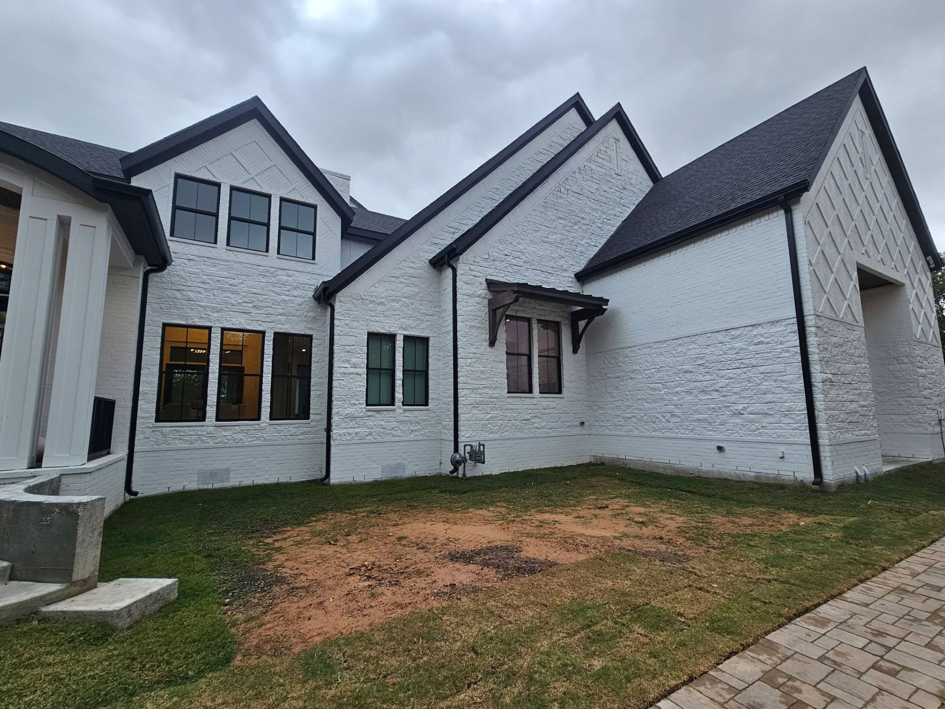 White brick house with black trim and roof, under cloudy sky. Green grass in front.