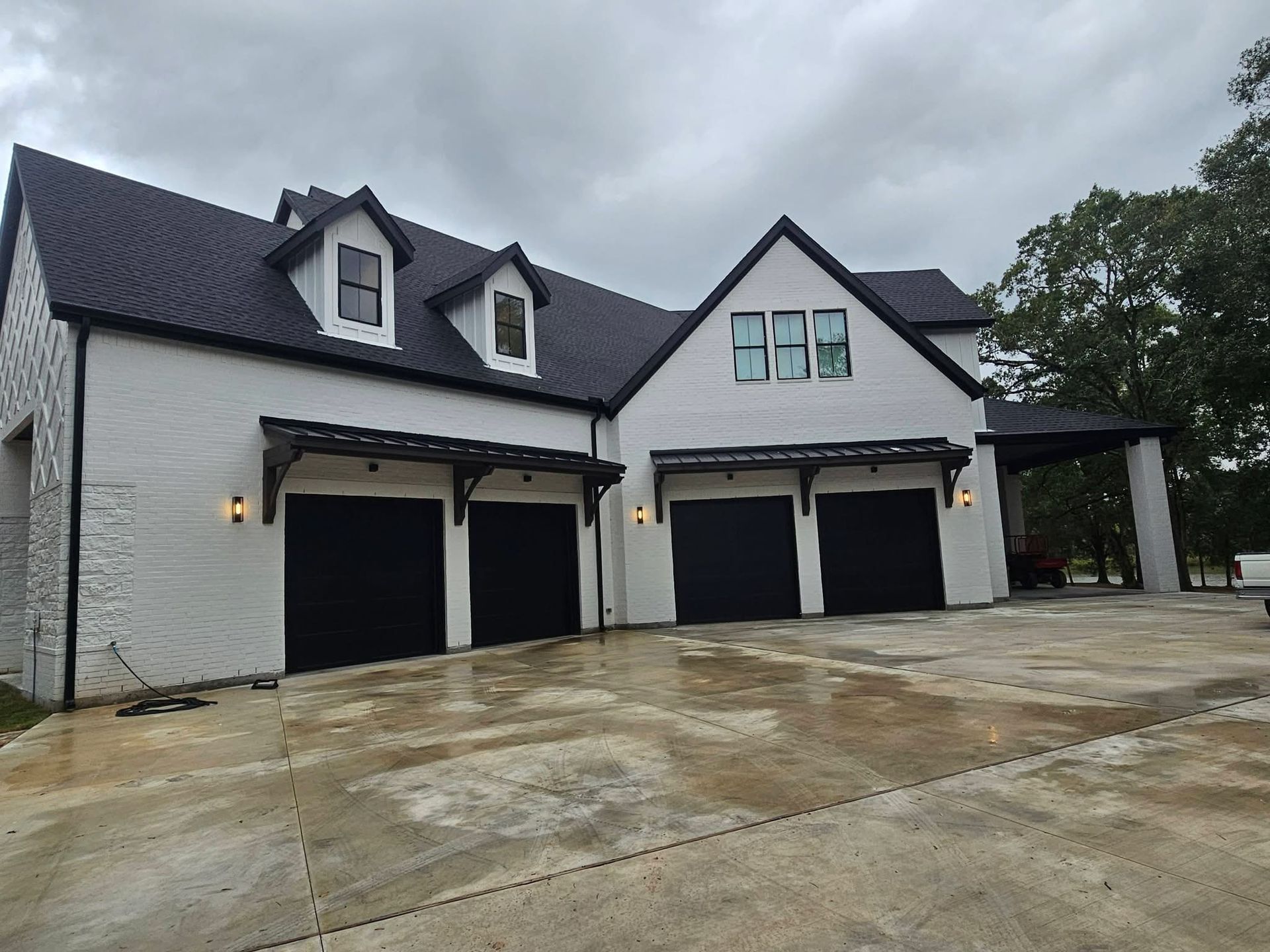 White house with black roof, garage doors, and awnings under a cloudy sky.