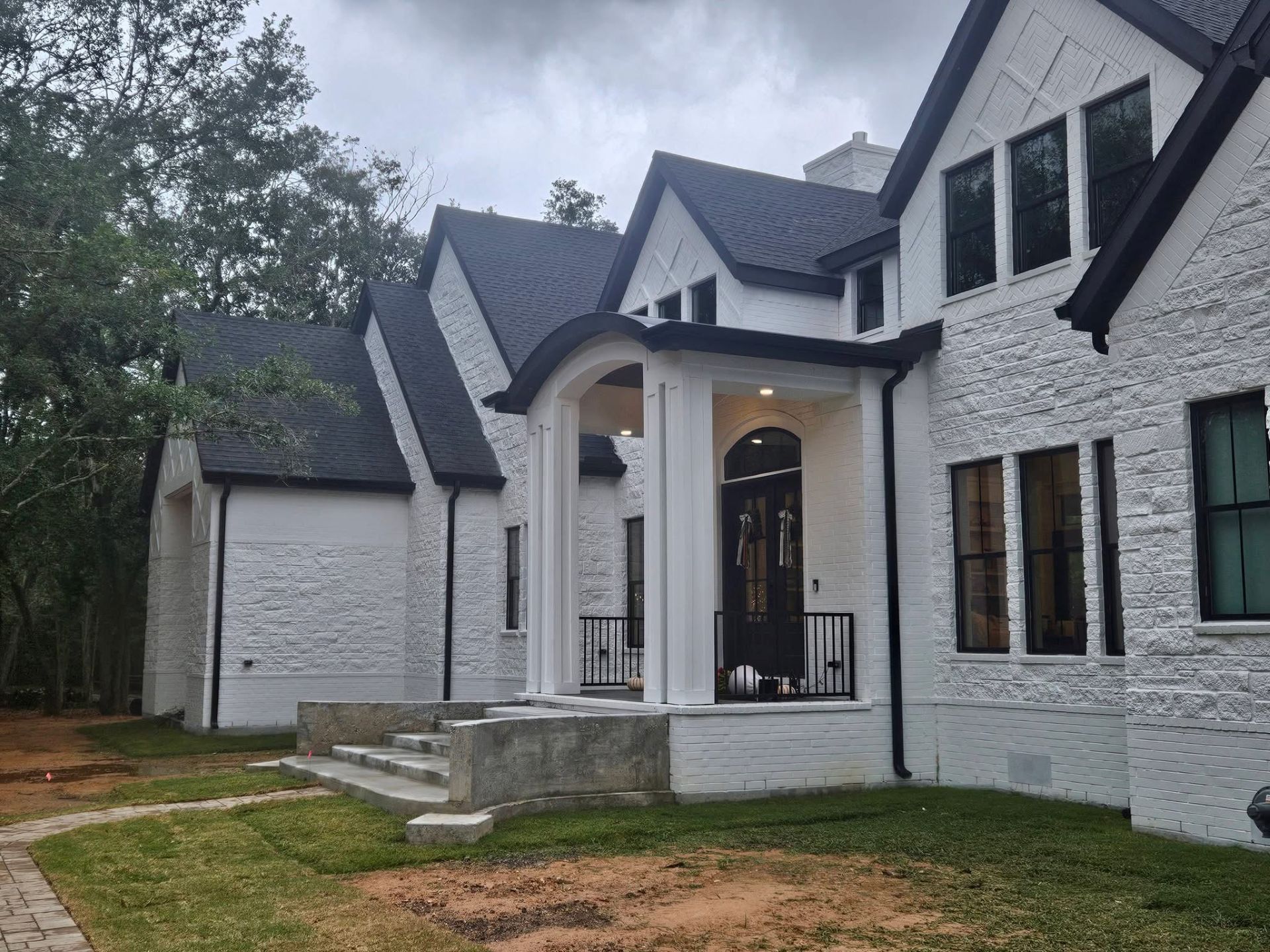 White brick house with black roof, arched entrance, and green lawn.