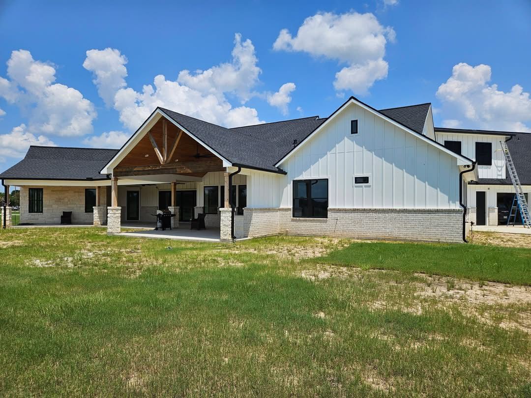 A modern, white-paneled house with black roof, large covered porch, and blue sky.