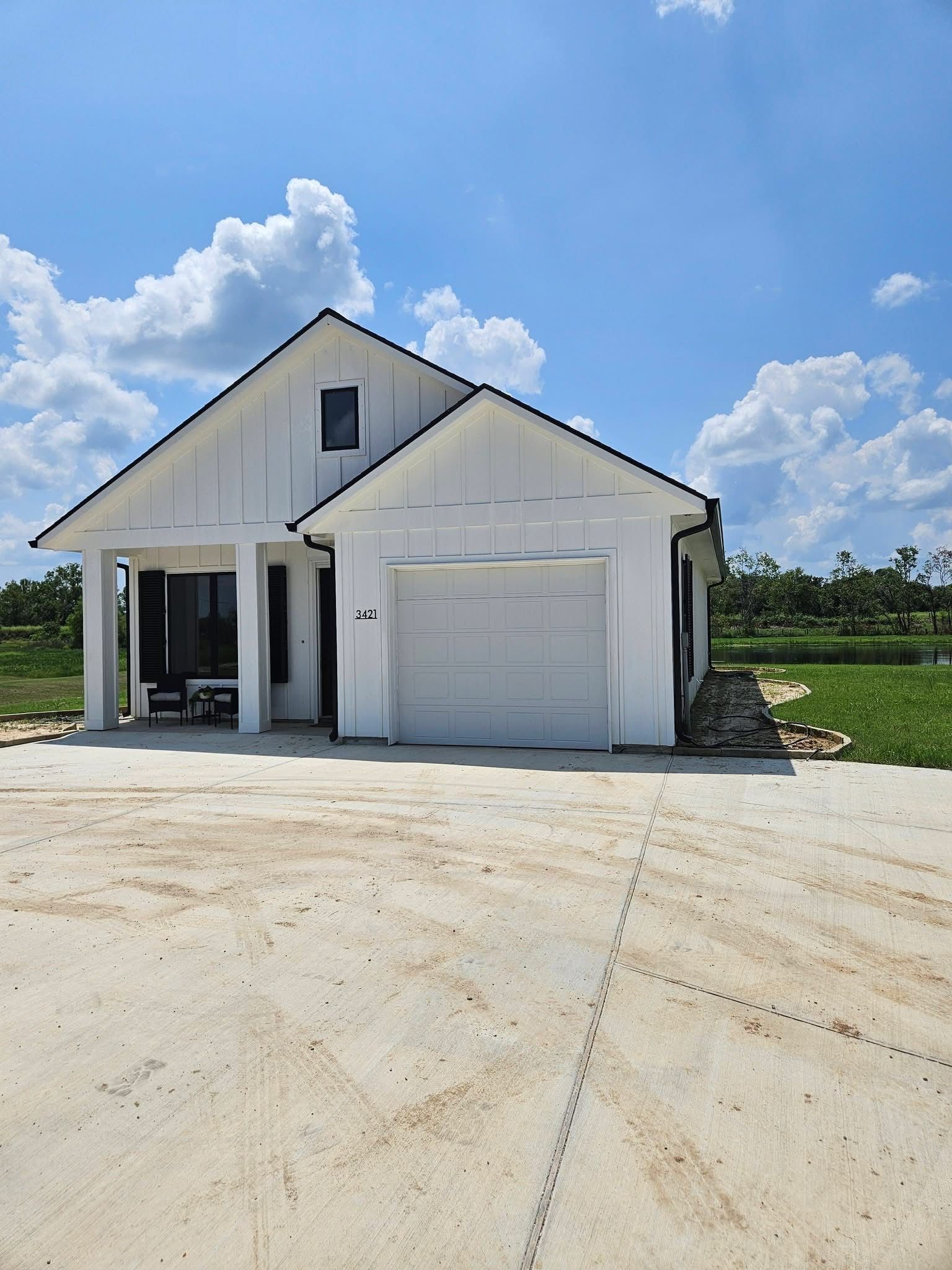 White farmhouse-style house with a garage, under construction, against a bright blue sky with clouds.