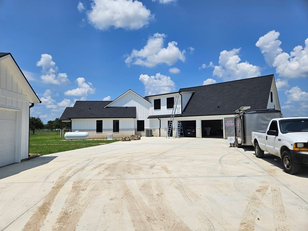 House under construction with white siding, black roof, and garage, under a blue sky.