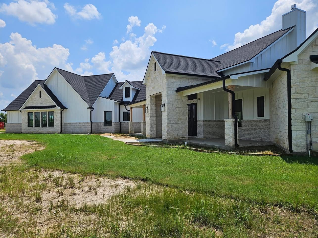 Modern house with white walls, black roof, and green lawn under a blue sky.