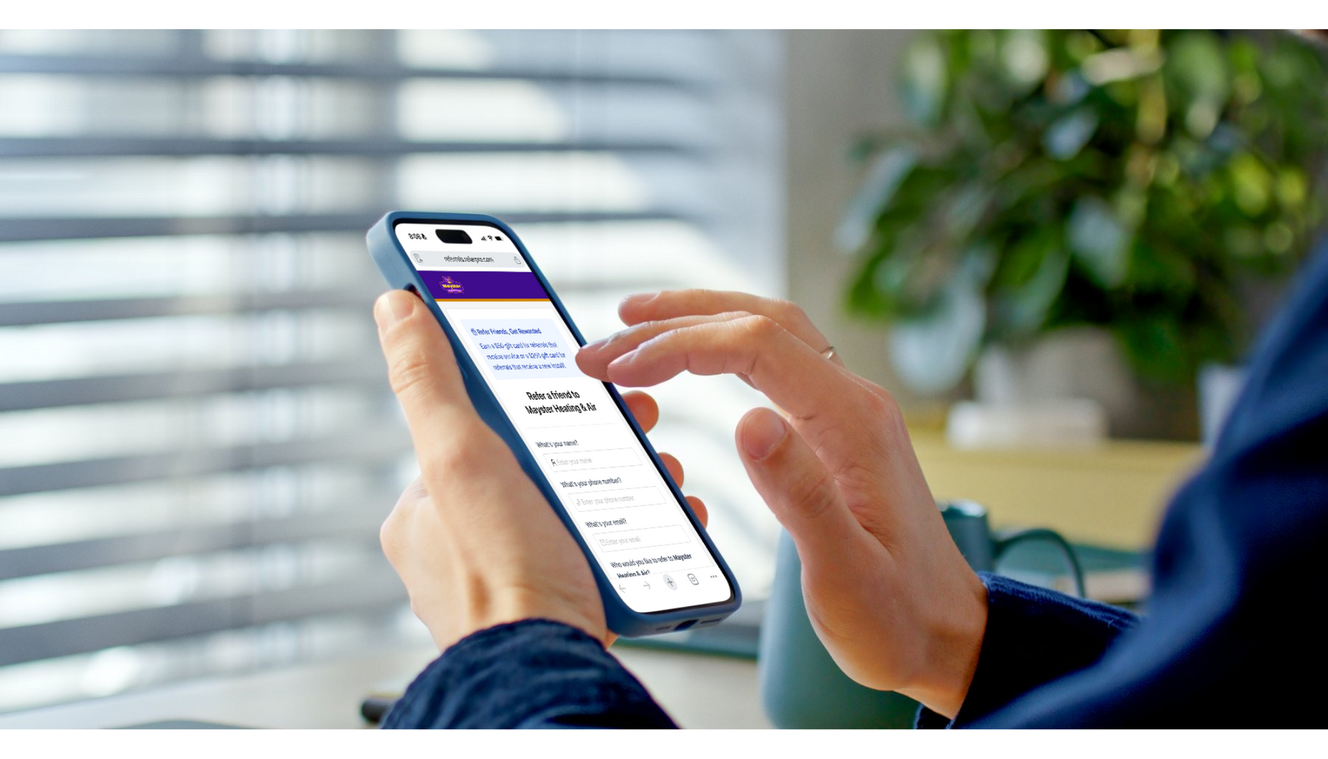 Person using a smartphone with a blue case, indoors near a window and plant, hands in focus.